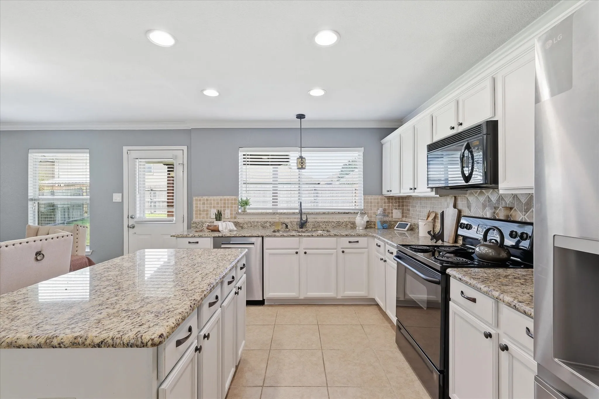 Kitchen featuring an expansive island with a polished stone countertop, white shaker-style cabinetry, mosaic tile backsplash, black appliances, and recessed lighting
