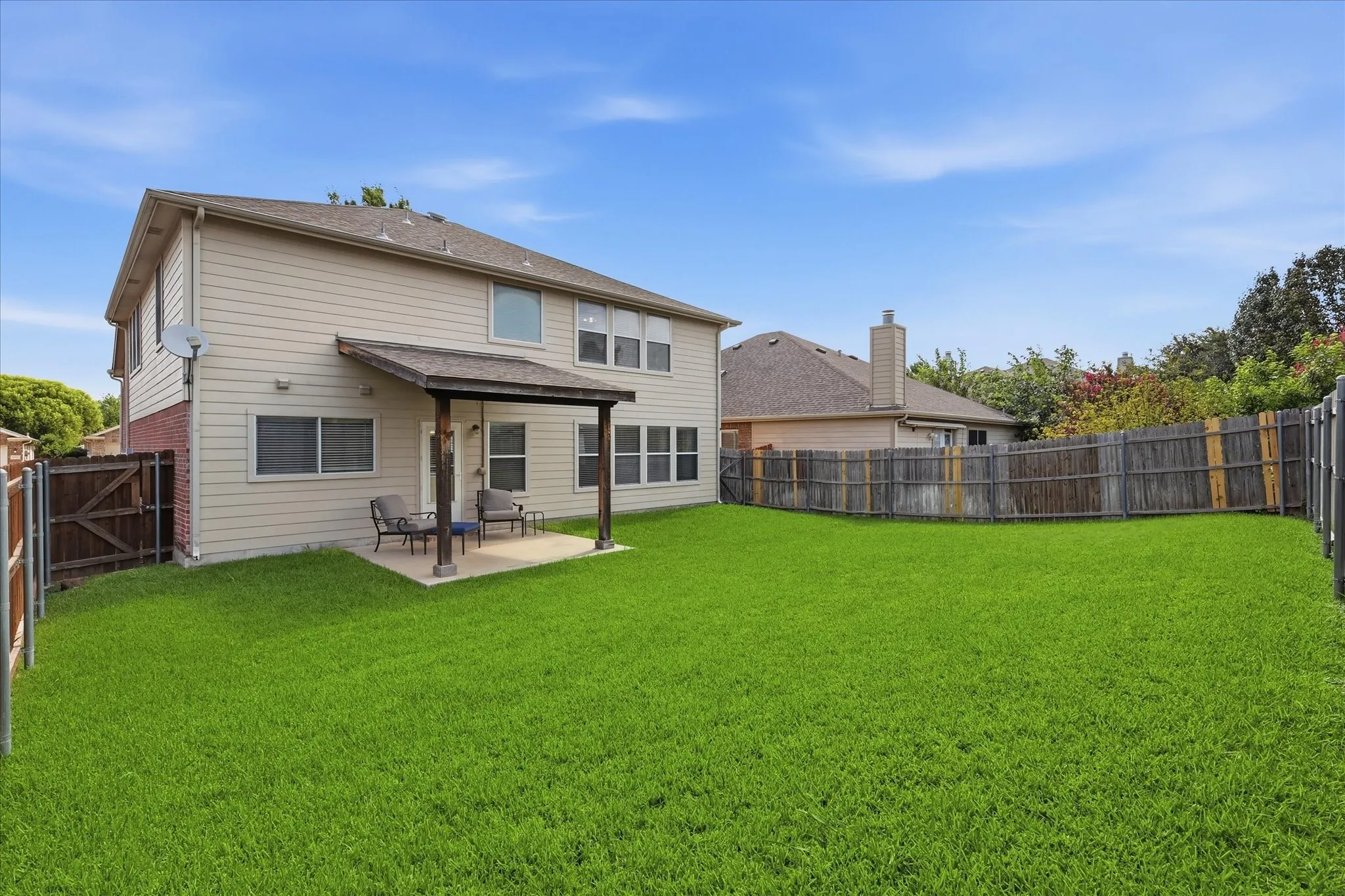 Expansive green lawn surrounds the property, featuring a covered patio and a privacy fence
