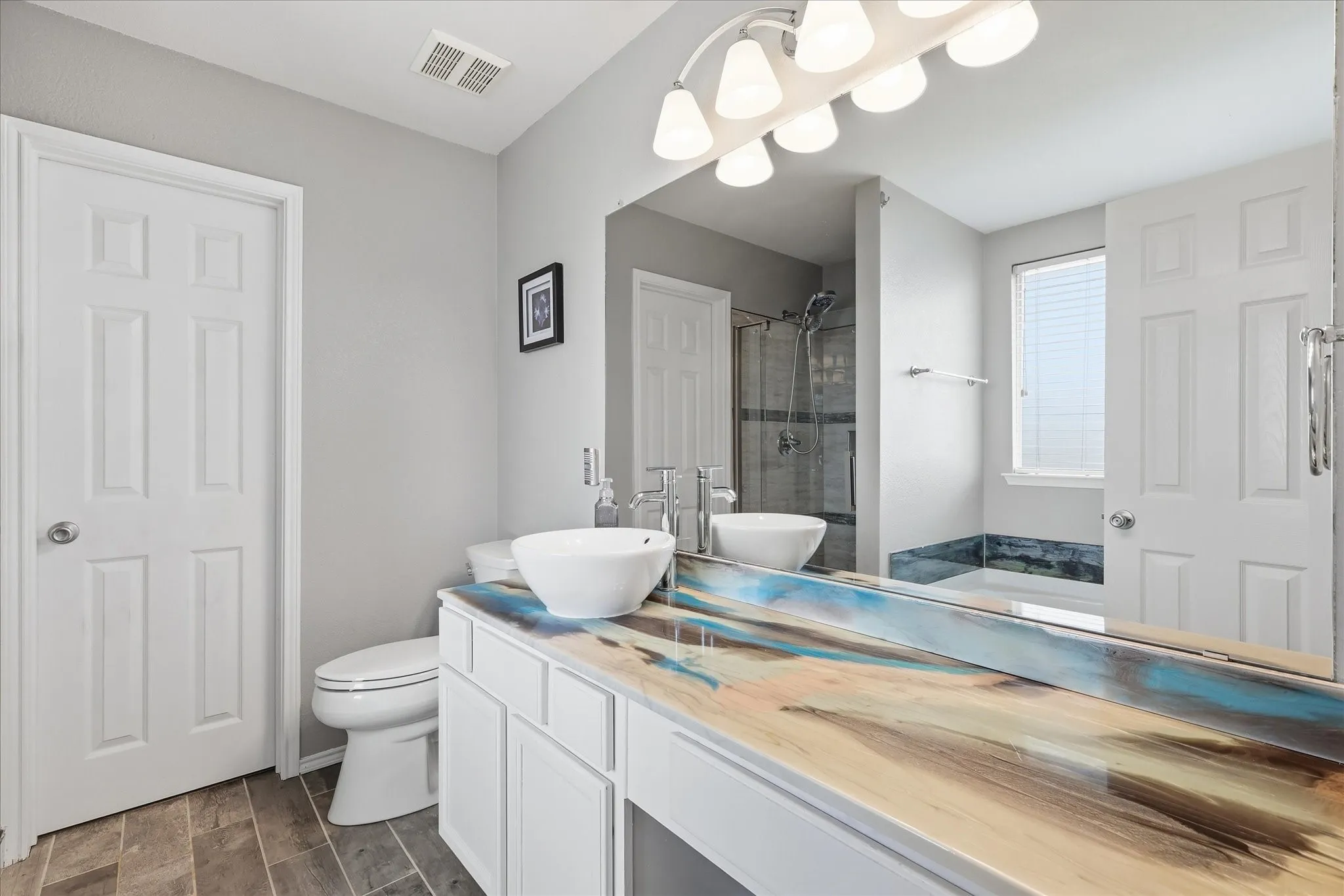 Bathroom featuring a vanity with a unique multi-toned countertop, a vessel sink, and wood-finish flooring