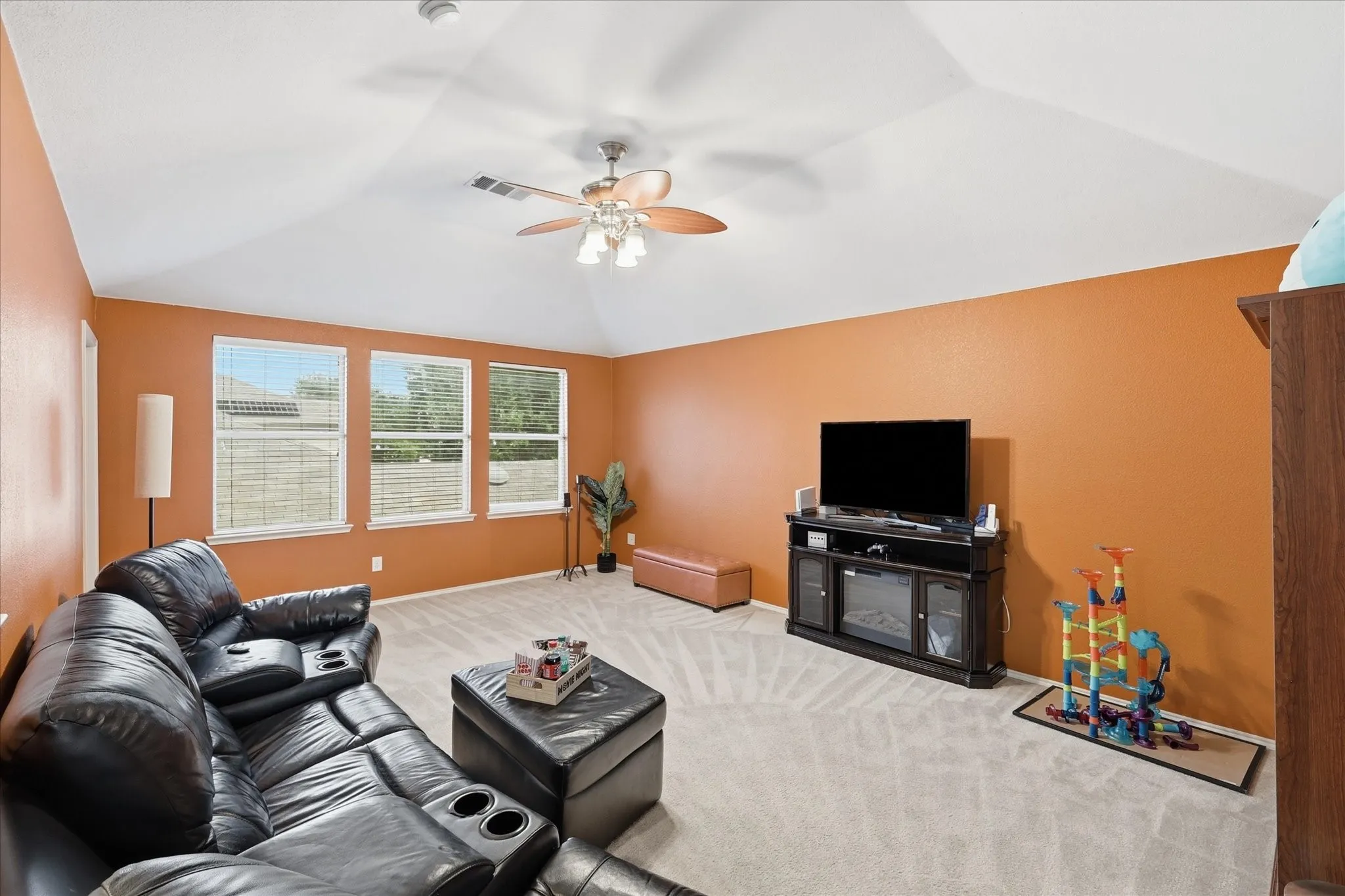 Spacious room featuring vaulted ceilings, light-toned carpet flooring, and three large windows with horizontal blinds