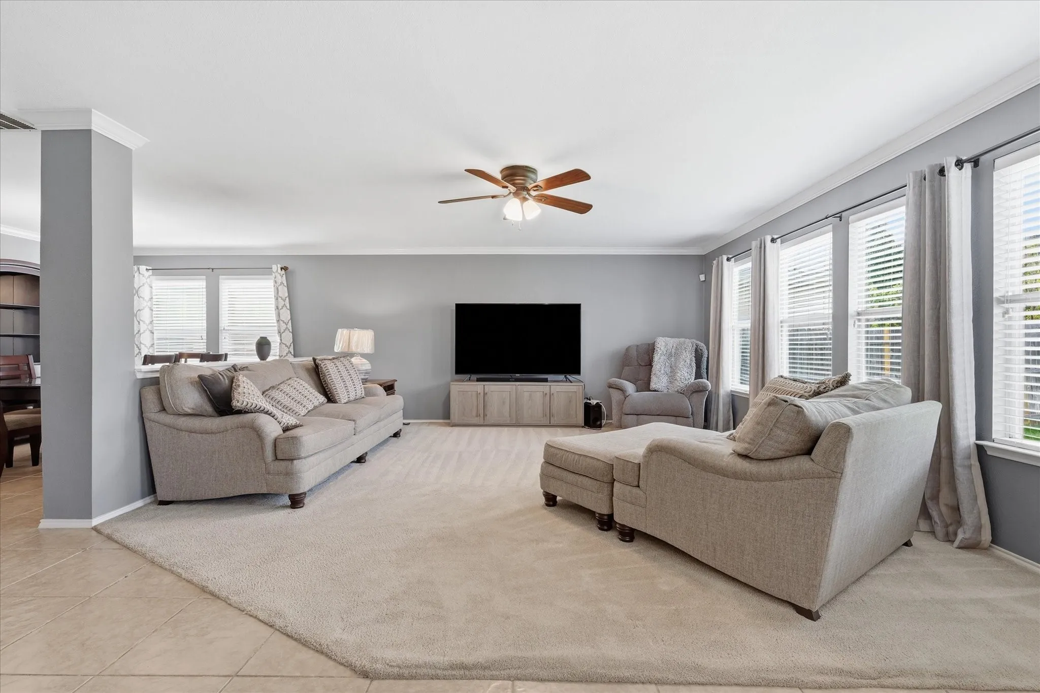 Spacious living area featuring neutral-toned walls, crown molding, and a ceiling fan with integrated lighting