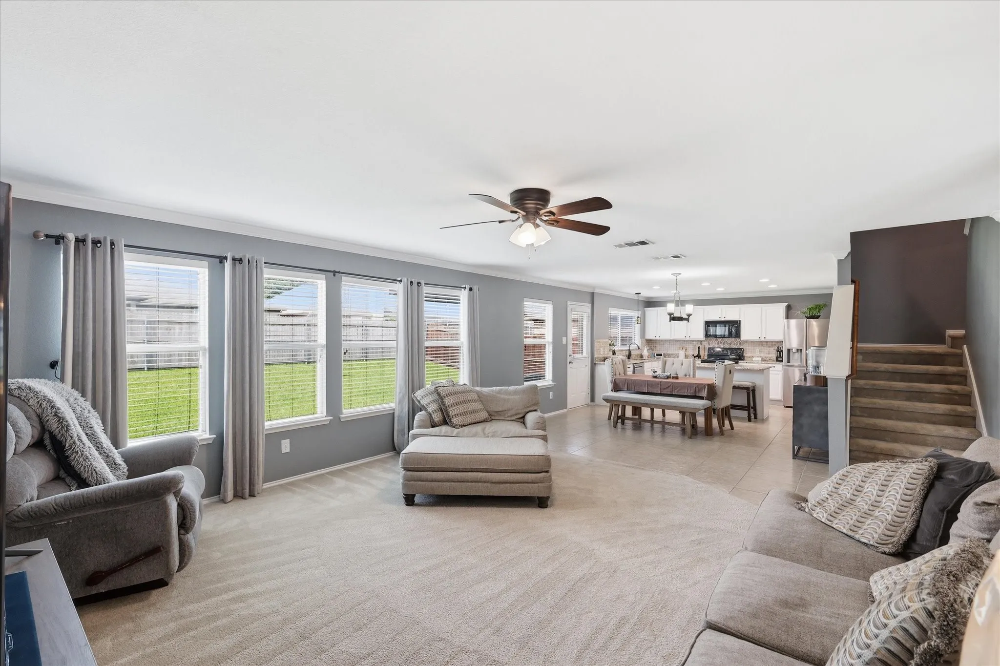 Open-concept living space with light-toned carpet and multiple windows