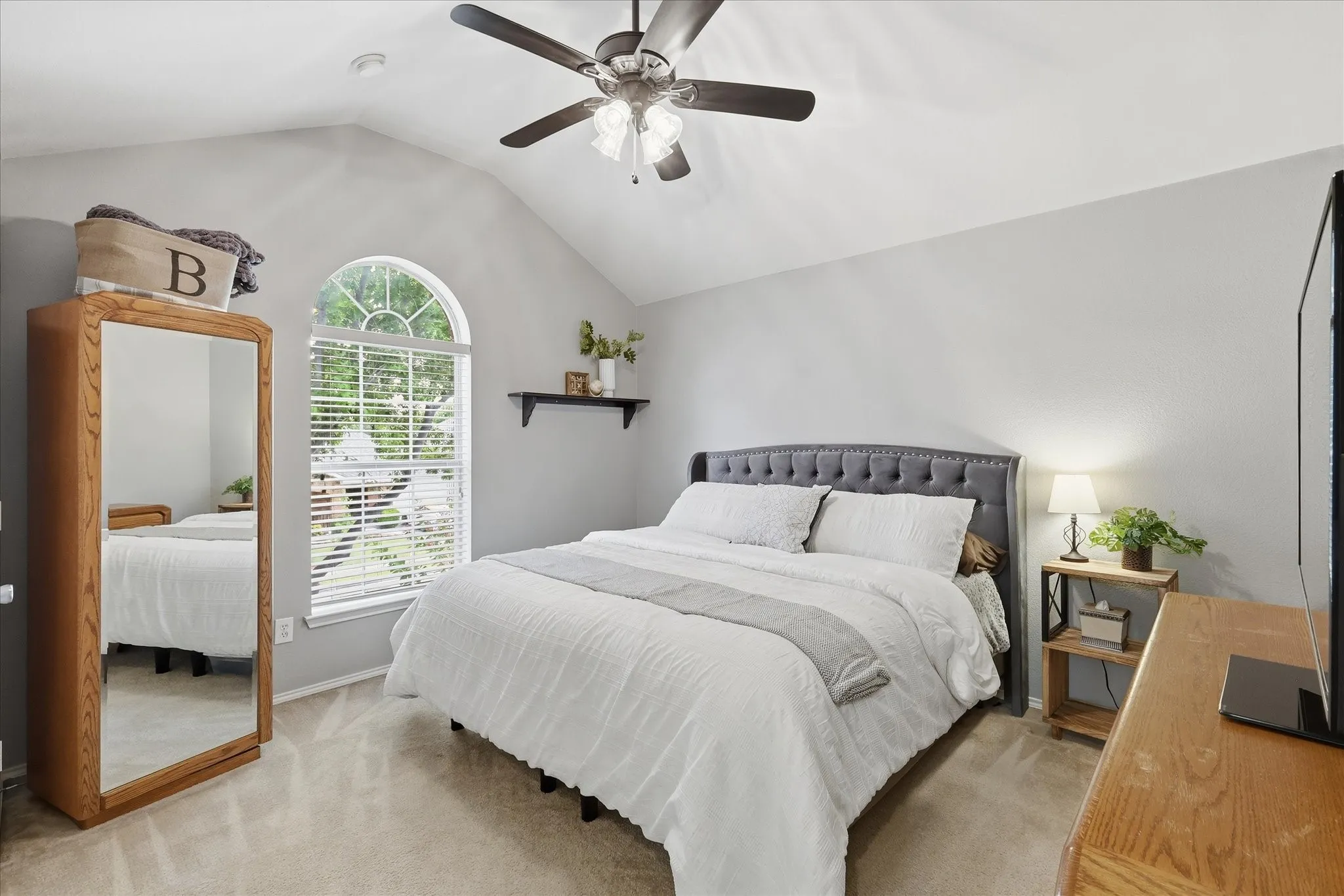 Bedroom featuring a vaulted ceiling with a ceiling fan, a large arched window with blinds, and light-toned carpeting accommodating a king bed