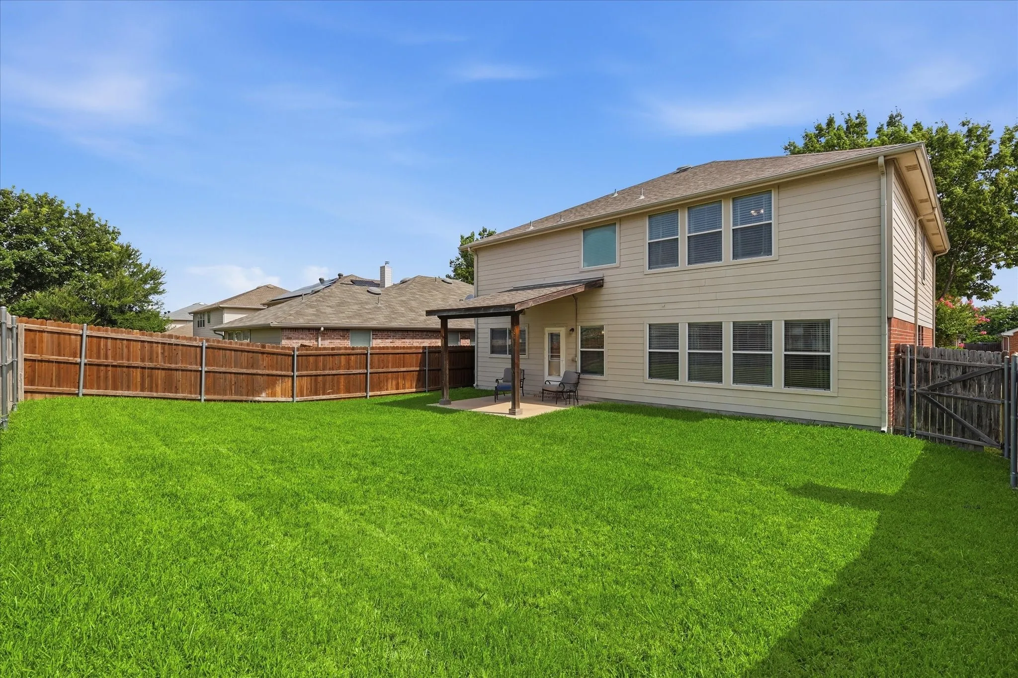 Expansive backyard featuring a lush lawn, privacy fencing, and a covered patio area