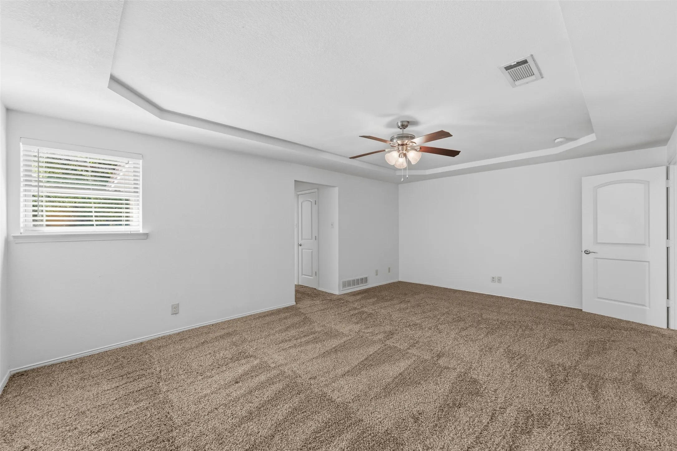 Spacious room with tray ceiling detailing, plush carpet flooring, and a ceiling fan with integrated lighting