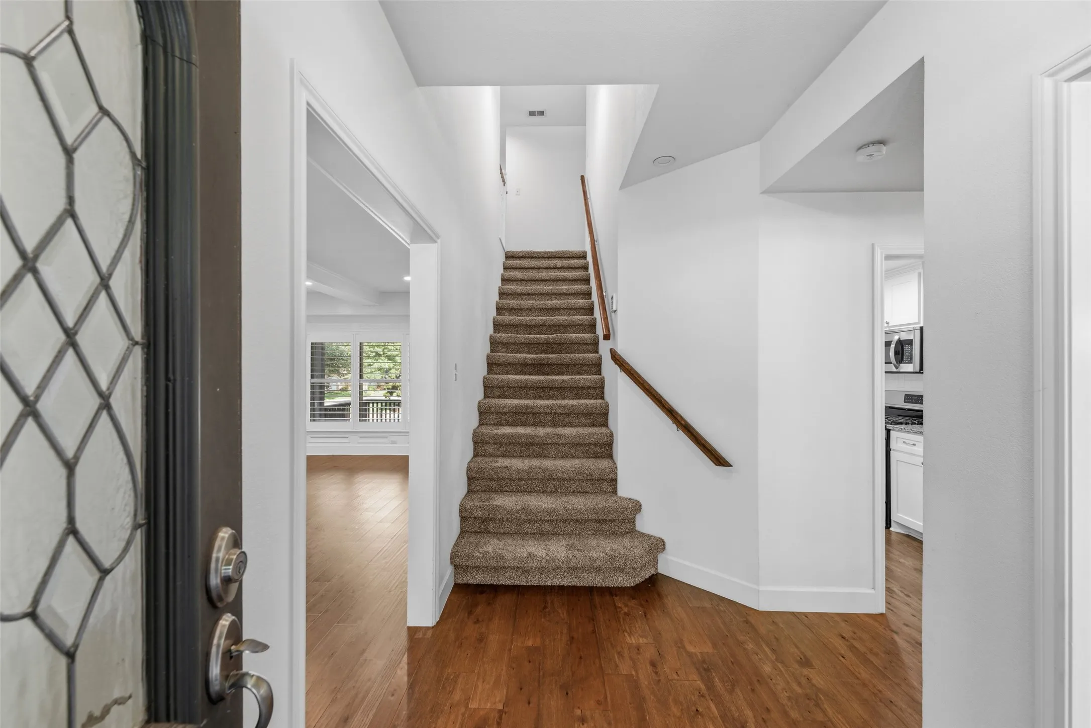Foyer featuring wood-finish flooring, a carpeted staircase with a wood handrail, and a leaded glass entry door