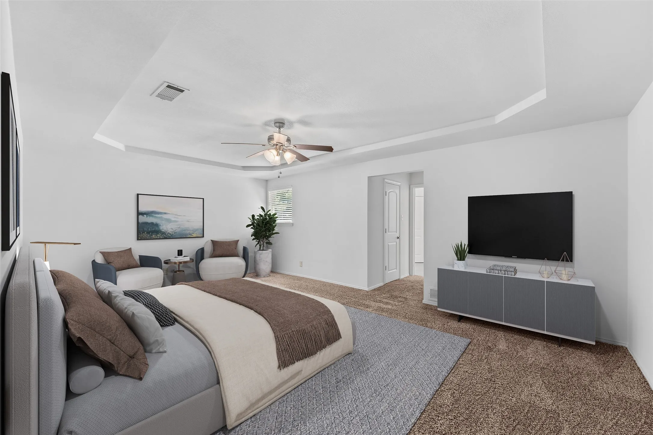 Spacious bedroom featuring a tray ceiling, ceiling fan, and light neutral carpet