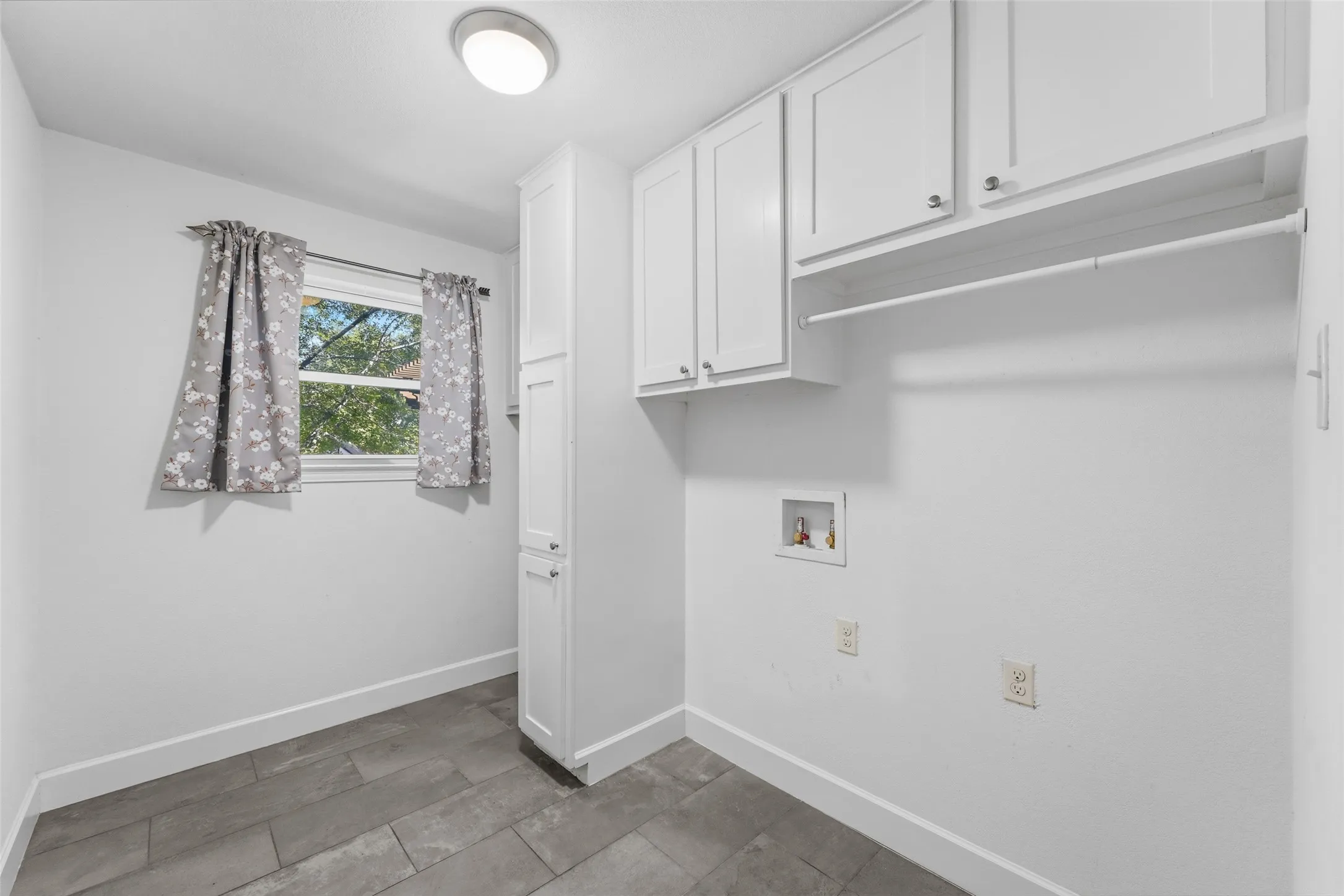 Utility area featuring wood-finish flooring, white cabinetry, a built-in hanging rod, and a window for natural light