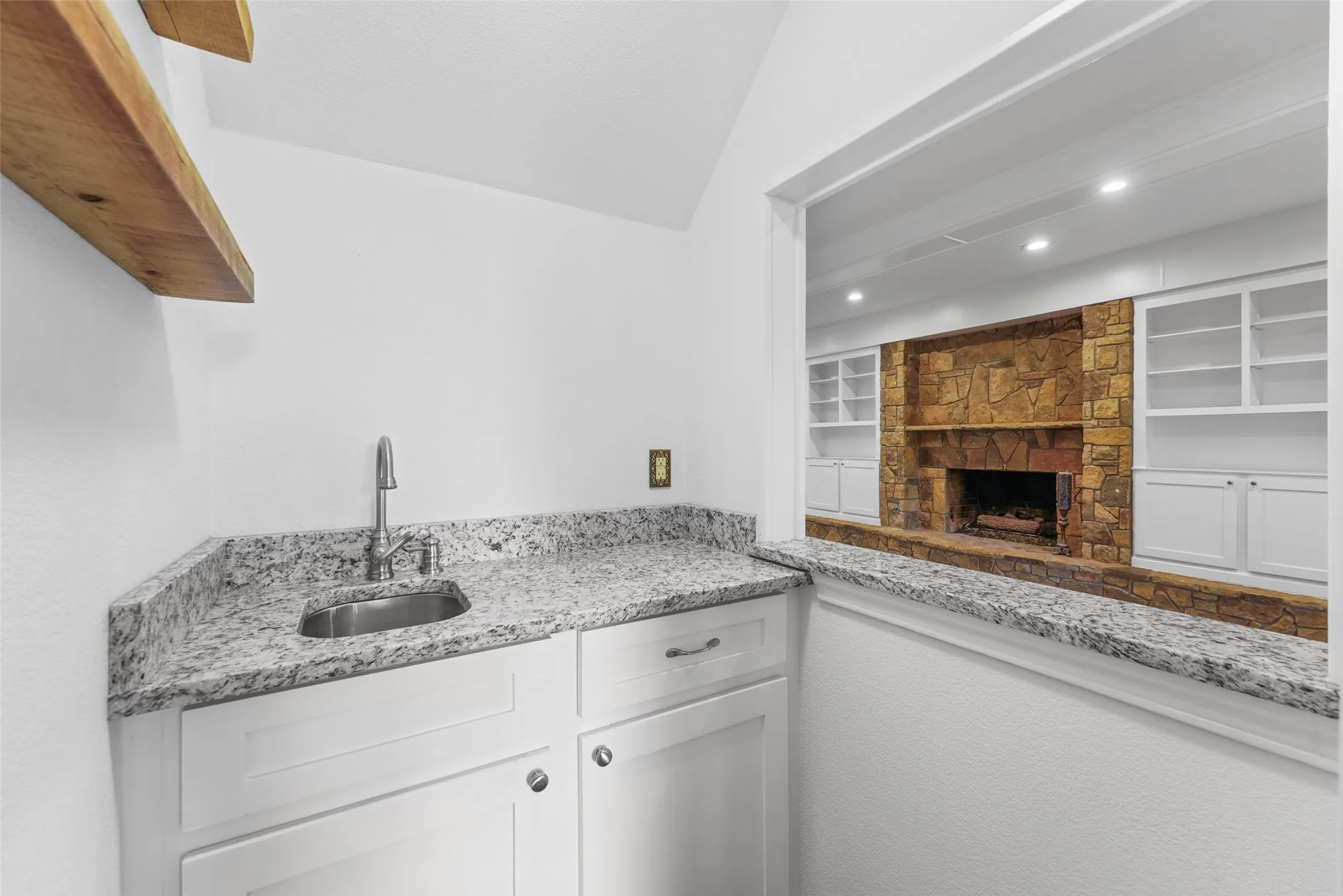 Wet bar featuring a stainless steel sink, contemporary faucet, white cabinetry, and a granite countertop