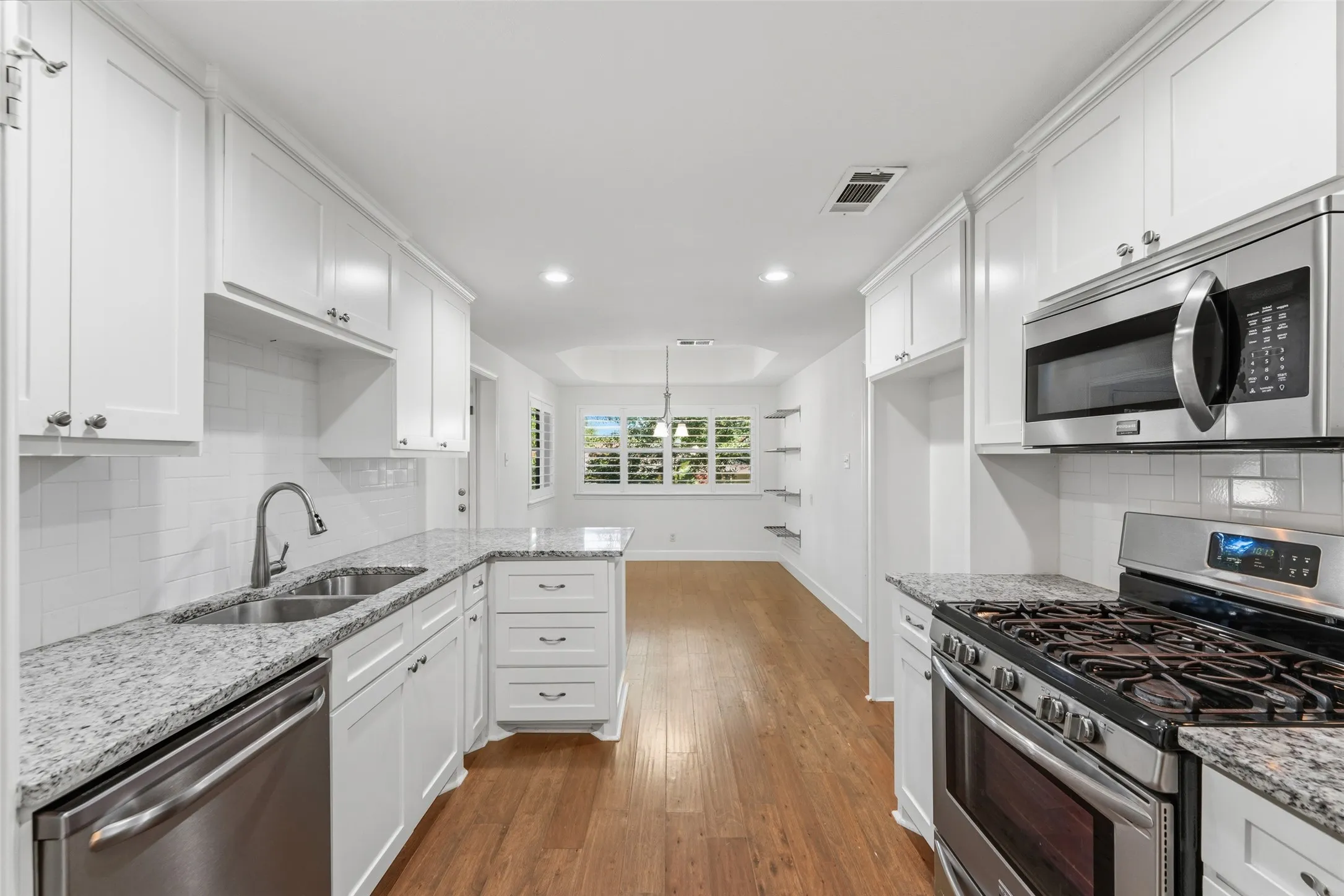 Bright kitchen featuring white cabinetry, stainless steel appliances, granite countertops, a subway tile backsplash, and wood-finish flooring