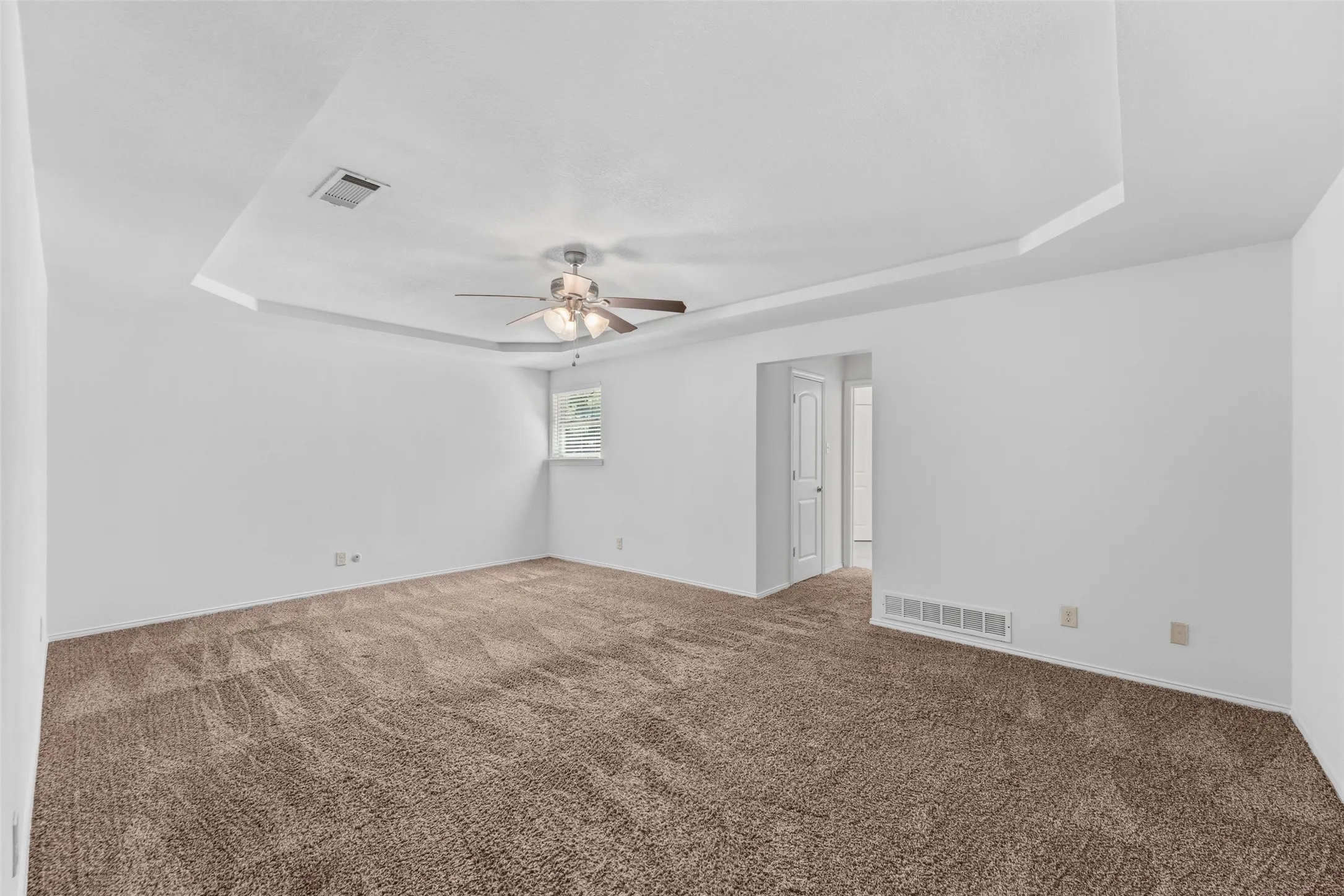 Spacious room with tray ceiling, ceiling fan, carpet flooring, and a single window