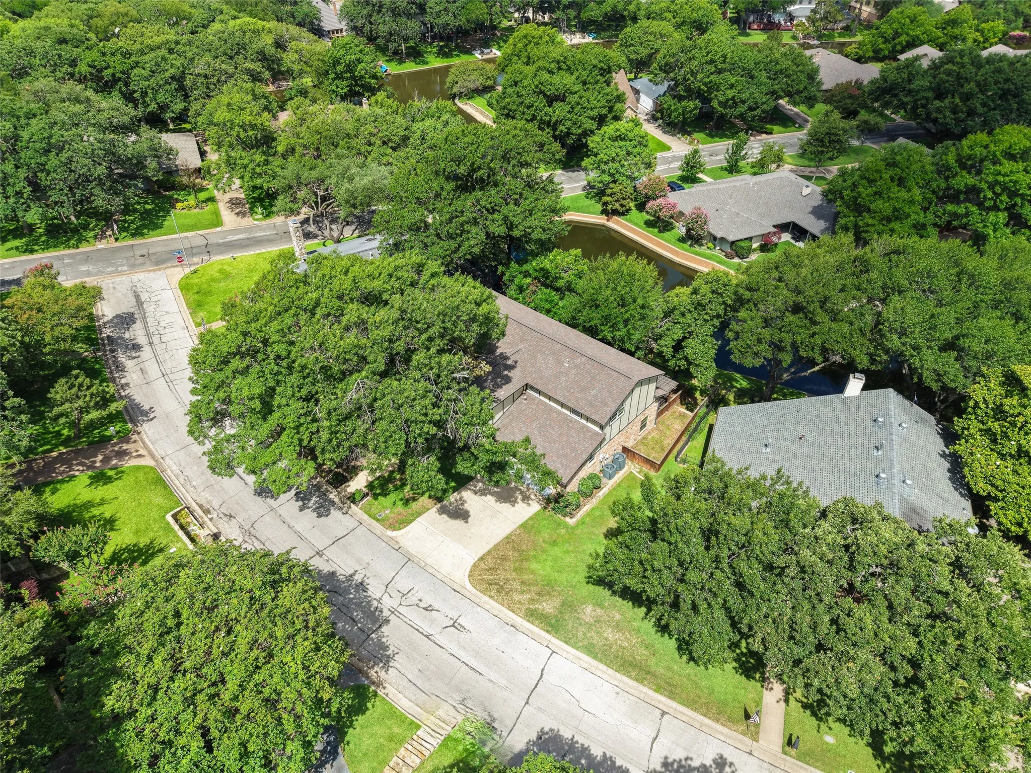 Aerial perspective showcasing a property surrounded by mature trees, featuring a gabled roof and a paved driveway