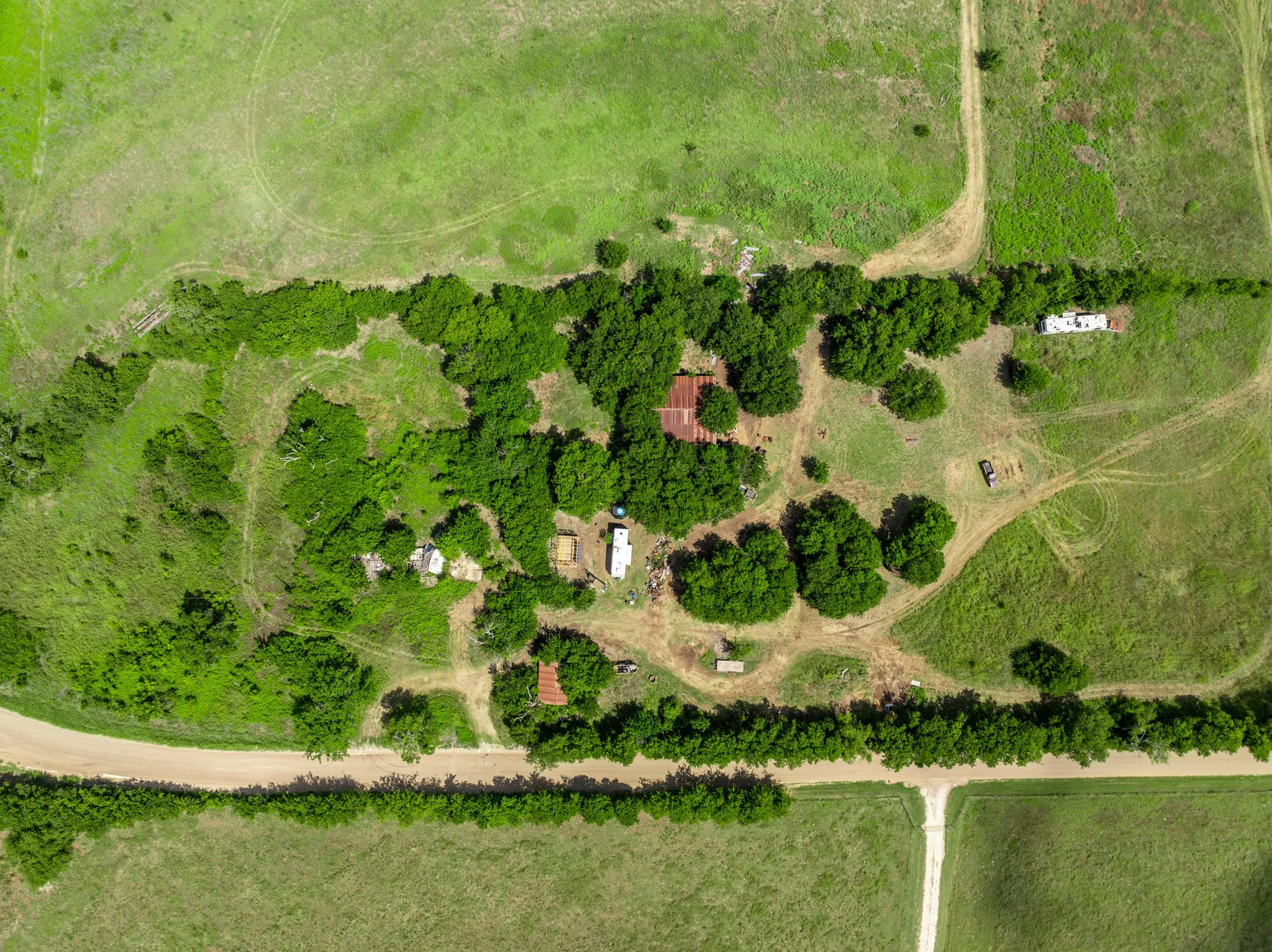 Expansive property featuring verdant green fields, multiple structures, established tree lines, and unpaved pathways