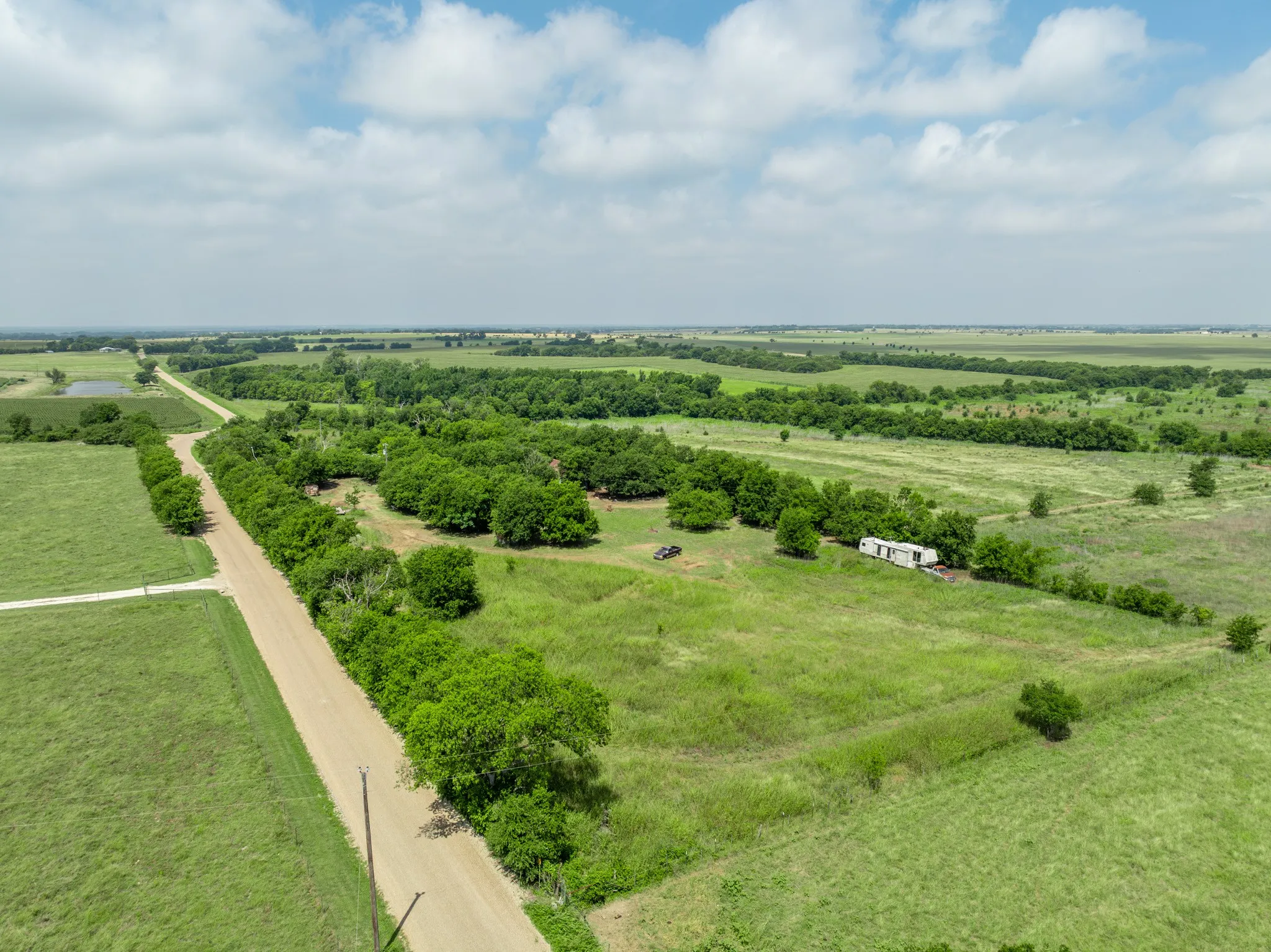 Expansive rural property featuring a long, unpaved road, mature tree lines, open grasslands, and a distant pond