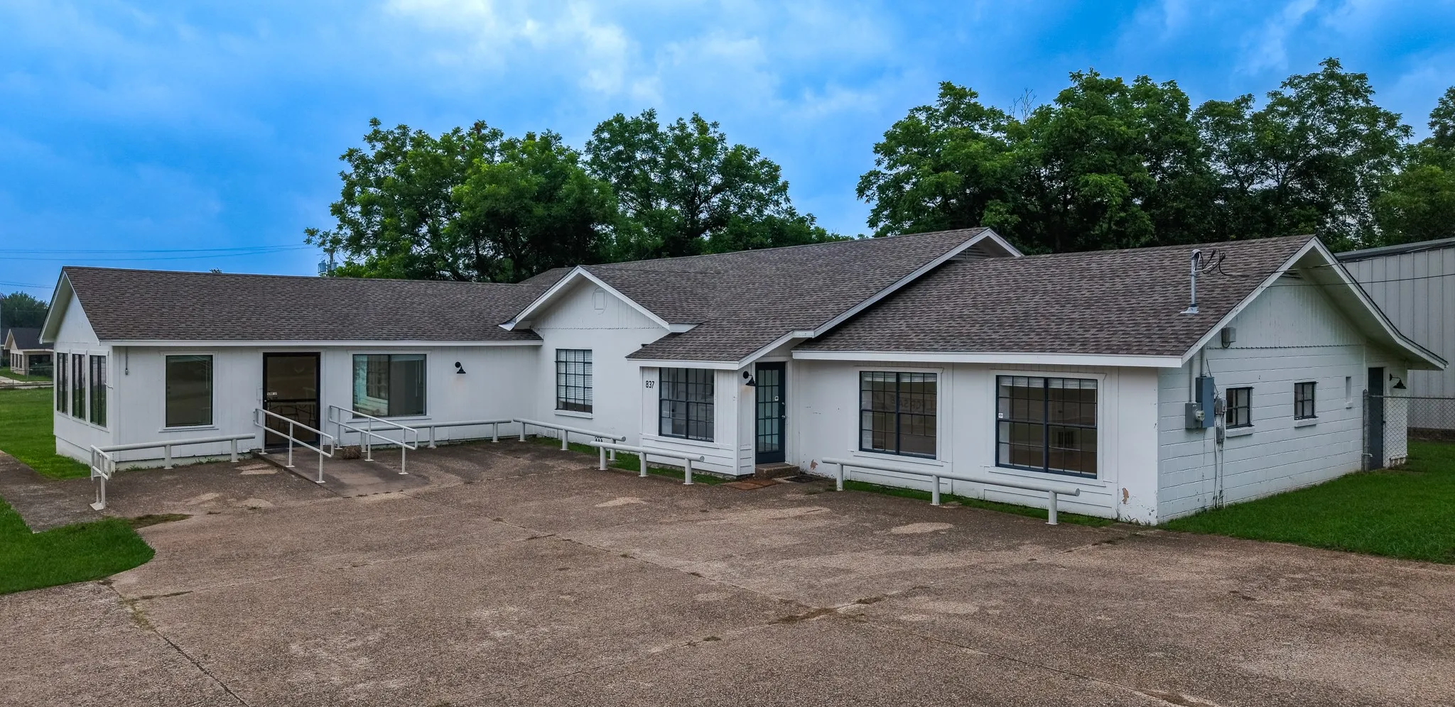 Single-story commercial building featuring multiple entry points, a dark shingle roof, and a white stucco exterior