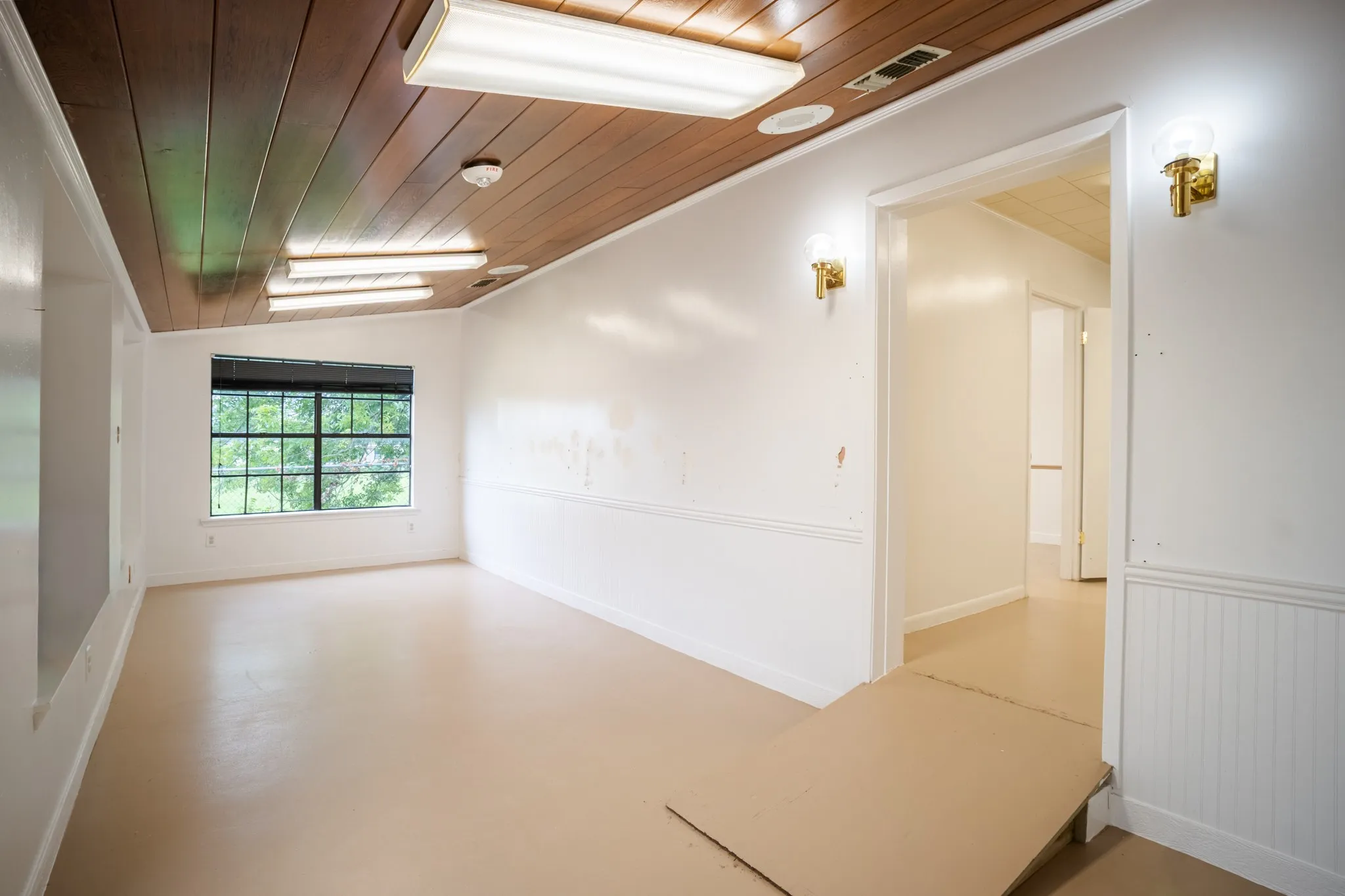 Interior space featuring light-toned flooring, white walls with wainscoting, and a wood-paneled ceiling
