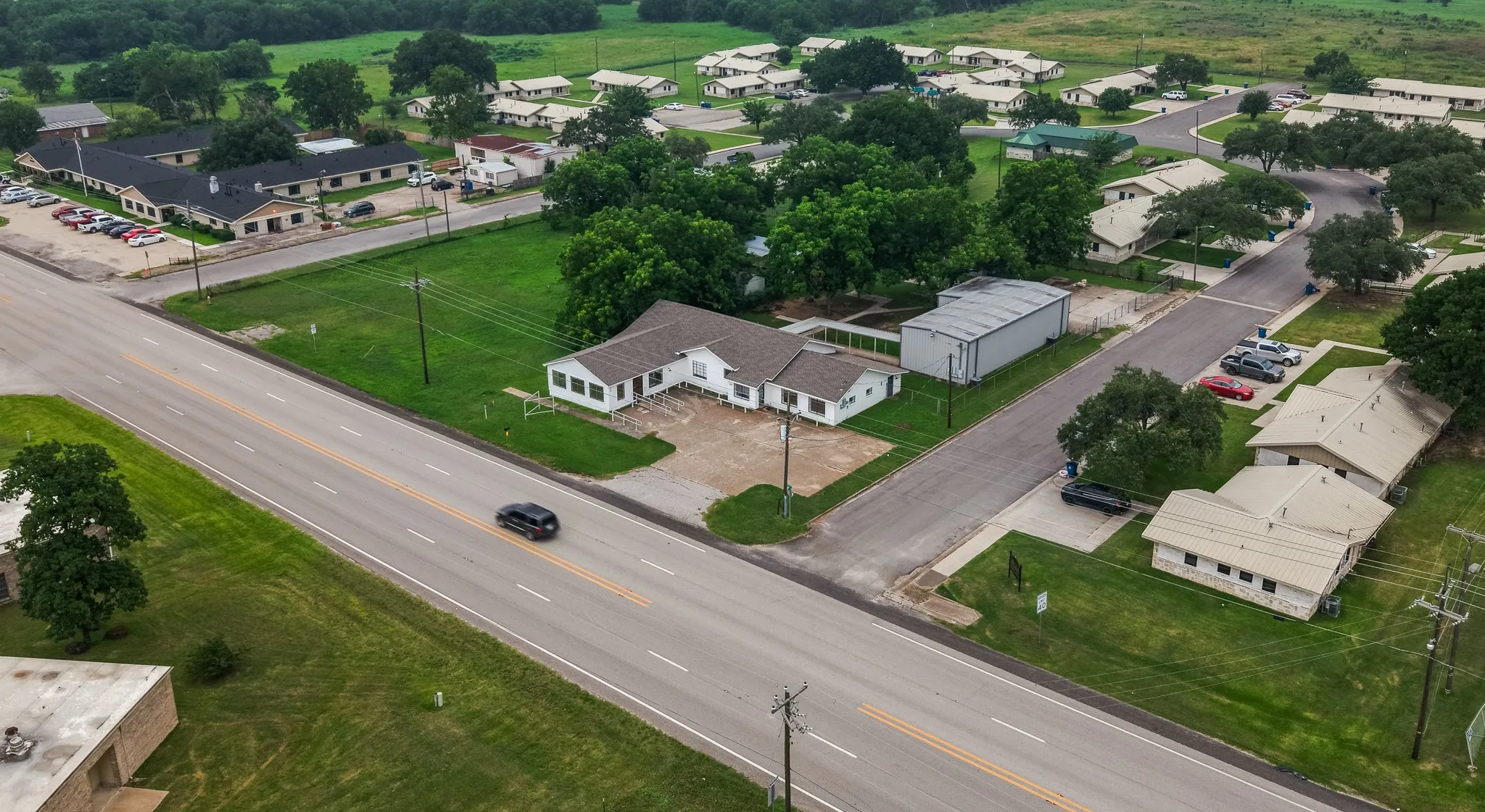 Aerial perspective showcasing a property with a primary single-story building featuring a light-colored exterior and a paved parking area