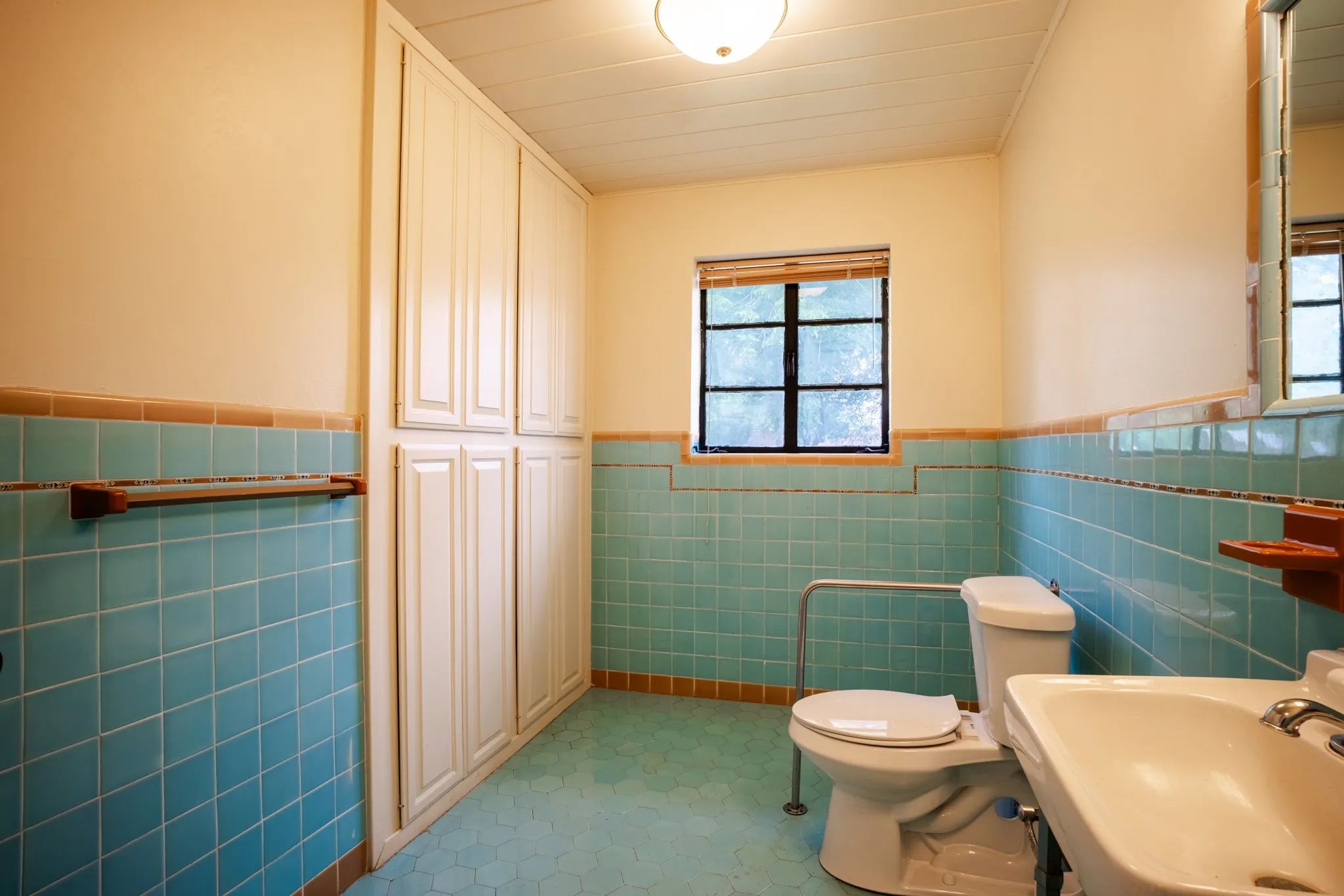Bathroom featuring full-height built-in cabinetry, aqua ceramic wall tiling, and a window with a wood-finish blind
