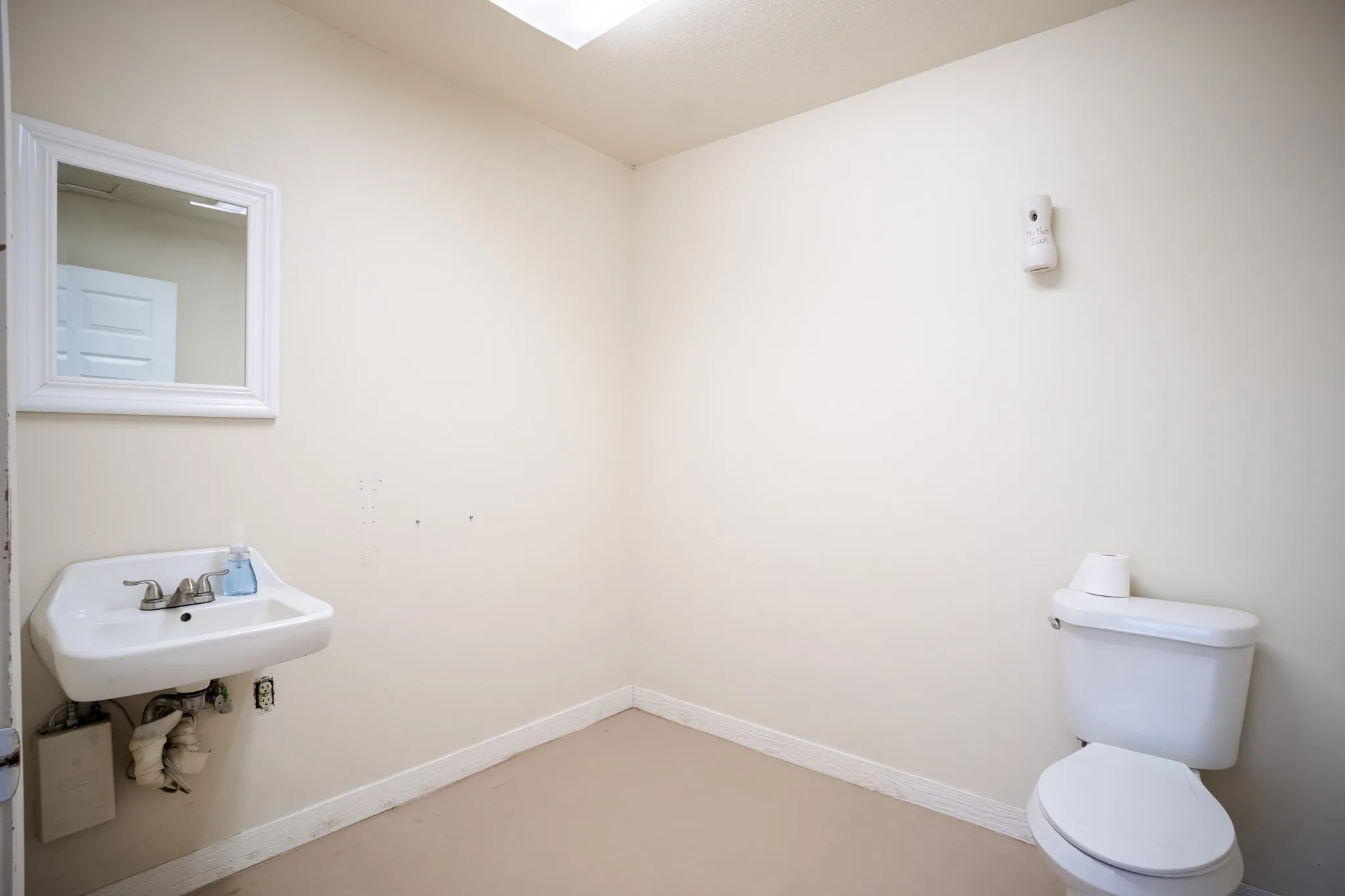 Powder room featuring a wall-mounted sink, a toilet, a framed mirror, and light-toned flooring