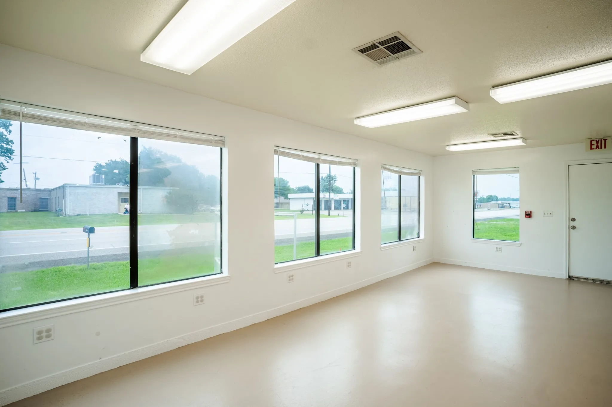 Spacious room featuring multiple large windows, neutral-toned flooring, white walls, and fluorescent overhead lighting