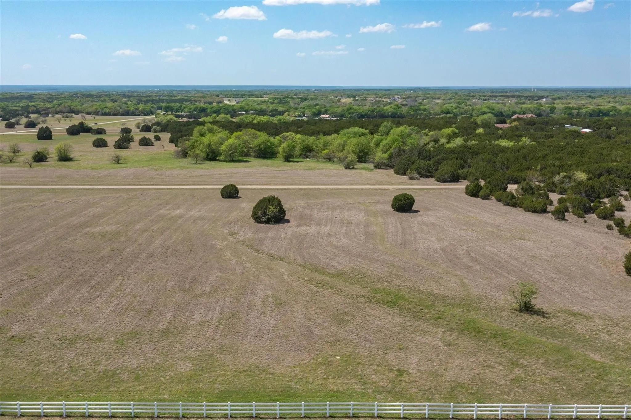 Expansive open land with scattered trees and a white multi-rail fence