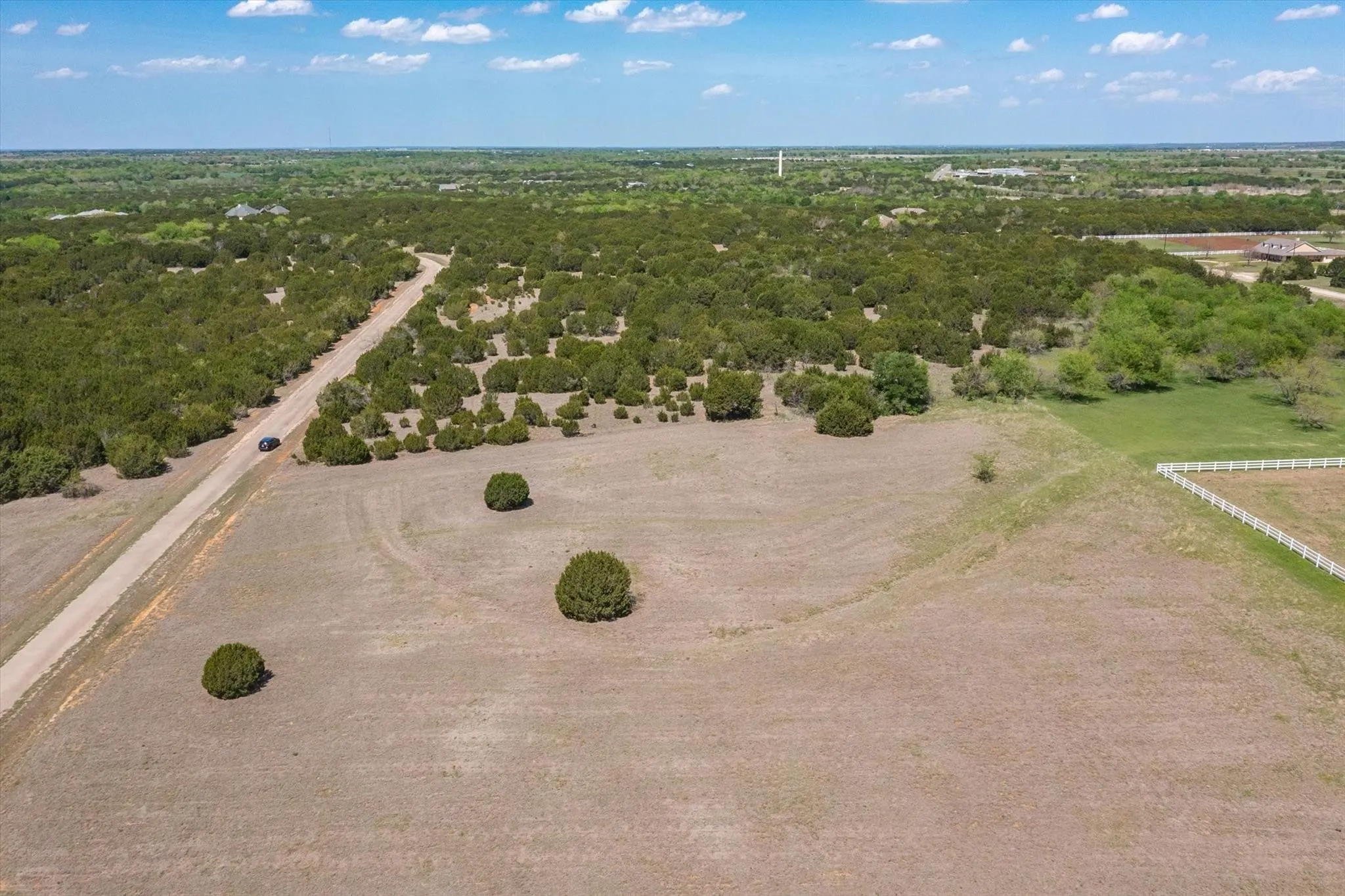 Expansive rural landscape featuring a private road, mature trees, open fields, and a white perimeter fence