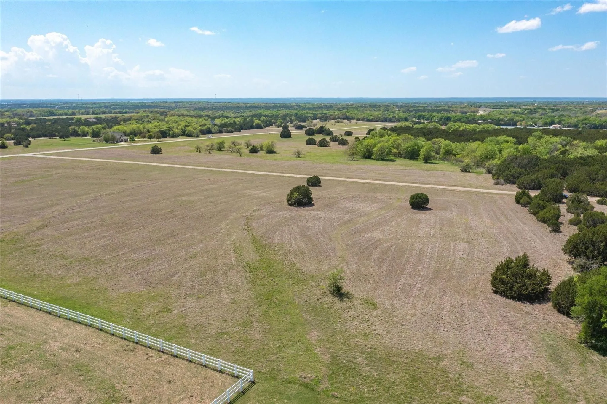 Expansive land parcel featuring a white ranch-style fence, scattered mature trees, and a tree line bordering the property