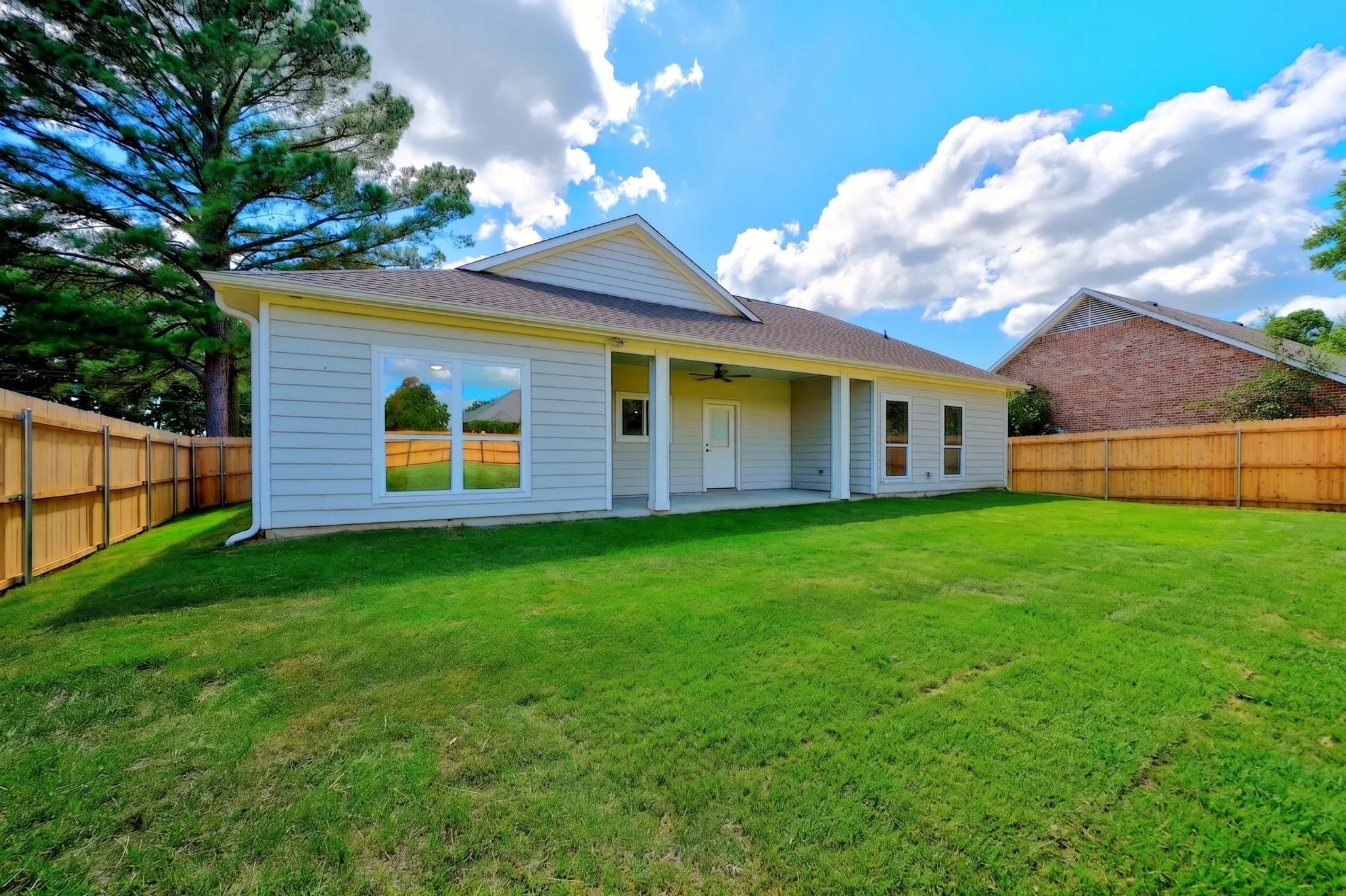 Expansive lawn with a wooden privacy fence, covered patio, and exterior siding
