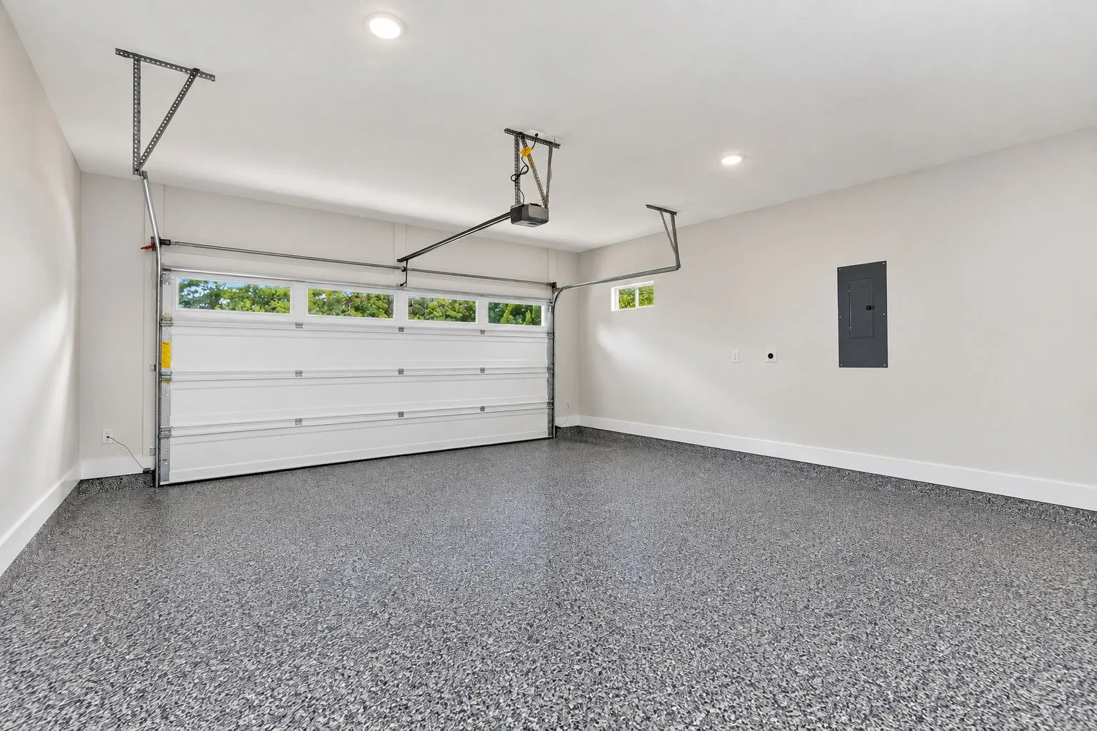 Spacious garage featuring a finished epoxy floor, white paneled garage door with upper windows, and a small transom window