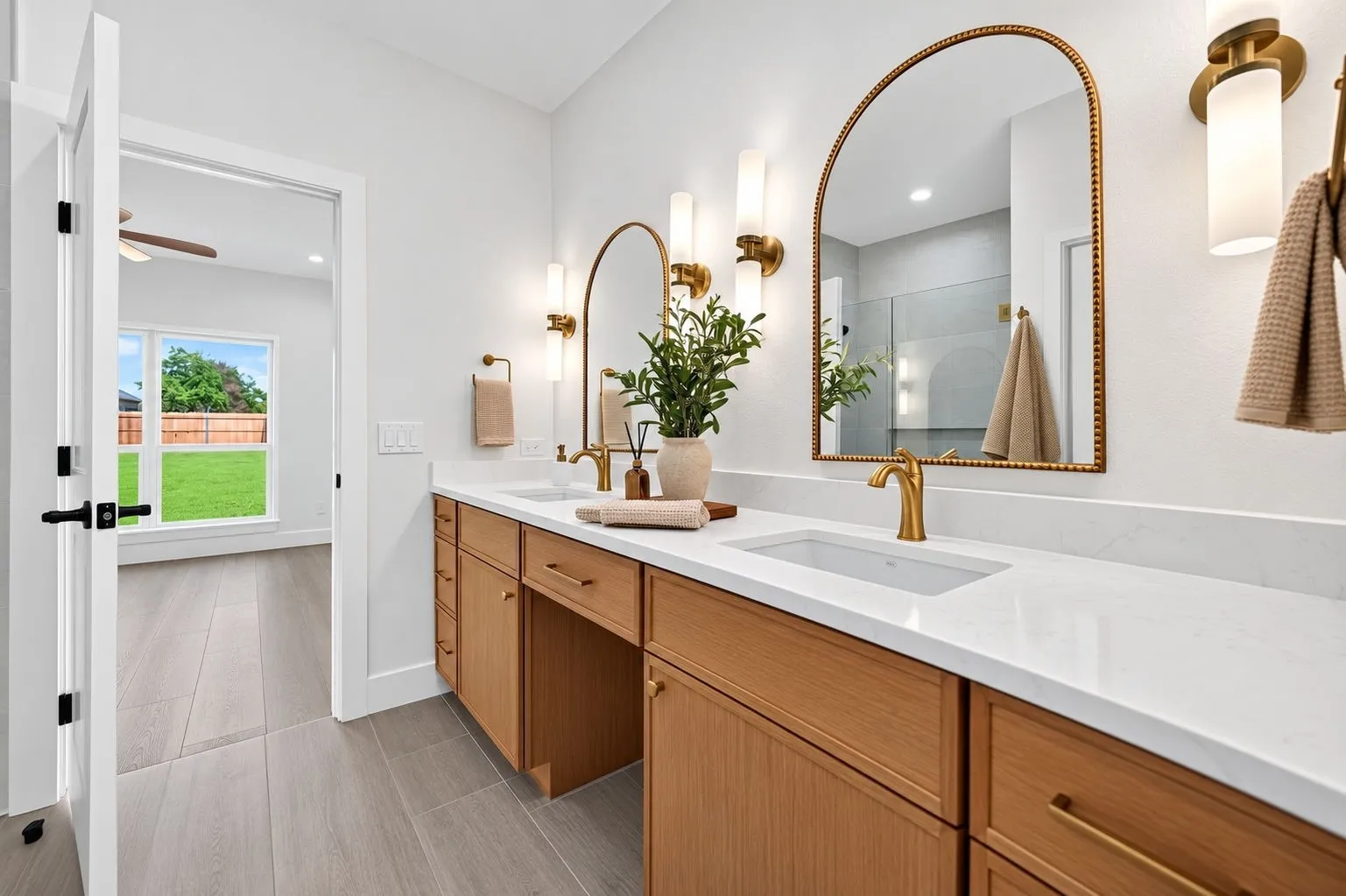 Dual vanity with light wood-finish cabinetry, white countertops, and gold-finish fixtures