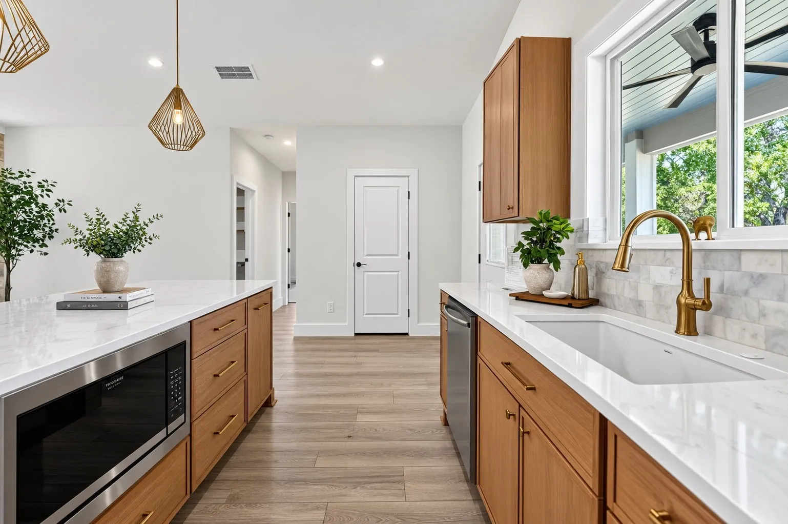 Kitchen featuring wood cabinetry, white countertops, built-in stainless steel microwave, large single-basin sink with gold-finish faucet, and coordinating gold-finish pendant lighting