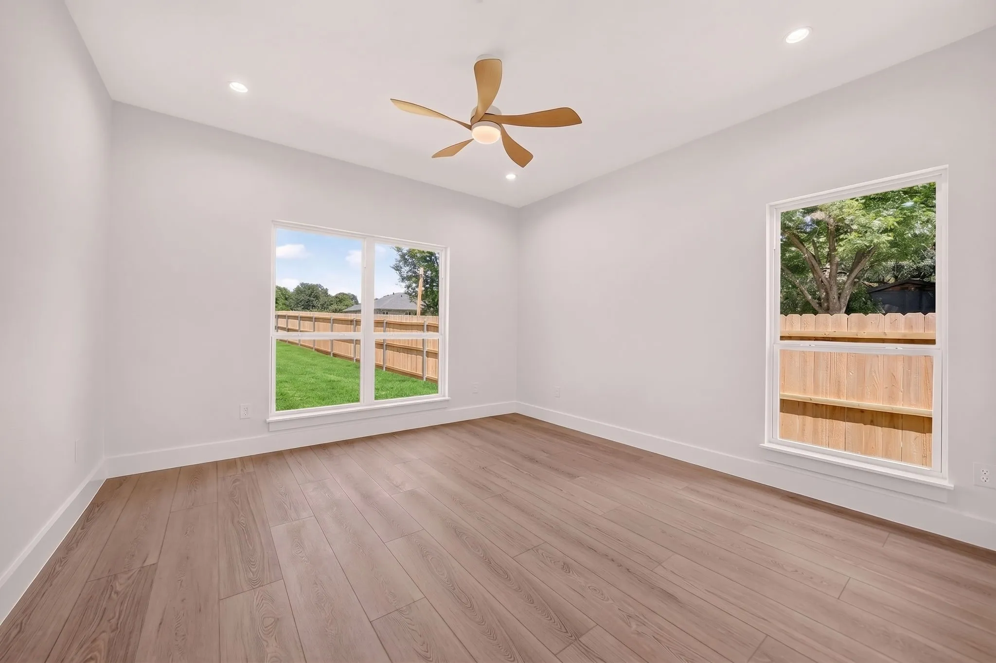 Spacious room featuring wood-finish flooring, white walls, multiple windows, recessed lighting, and a ceiling fan