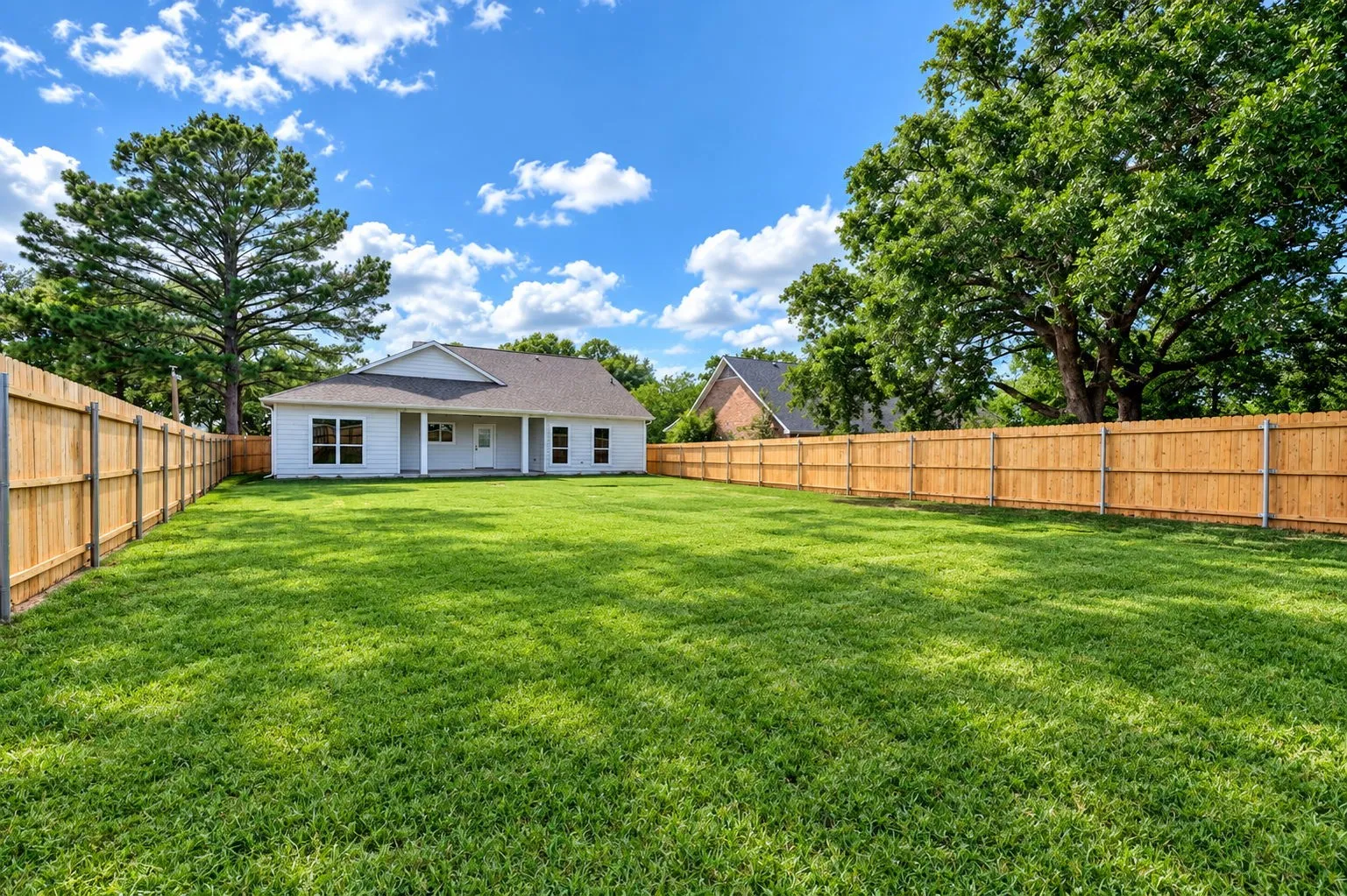 Expansive backyard featuring a manicured lawn, full perimeter wood fencing, and mature trees