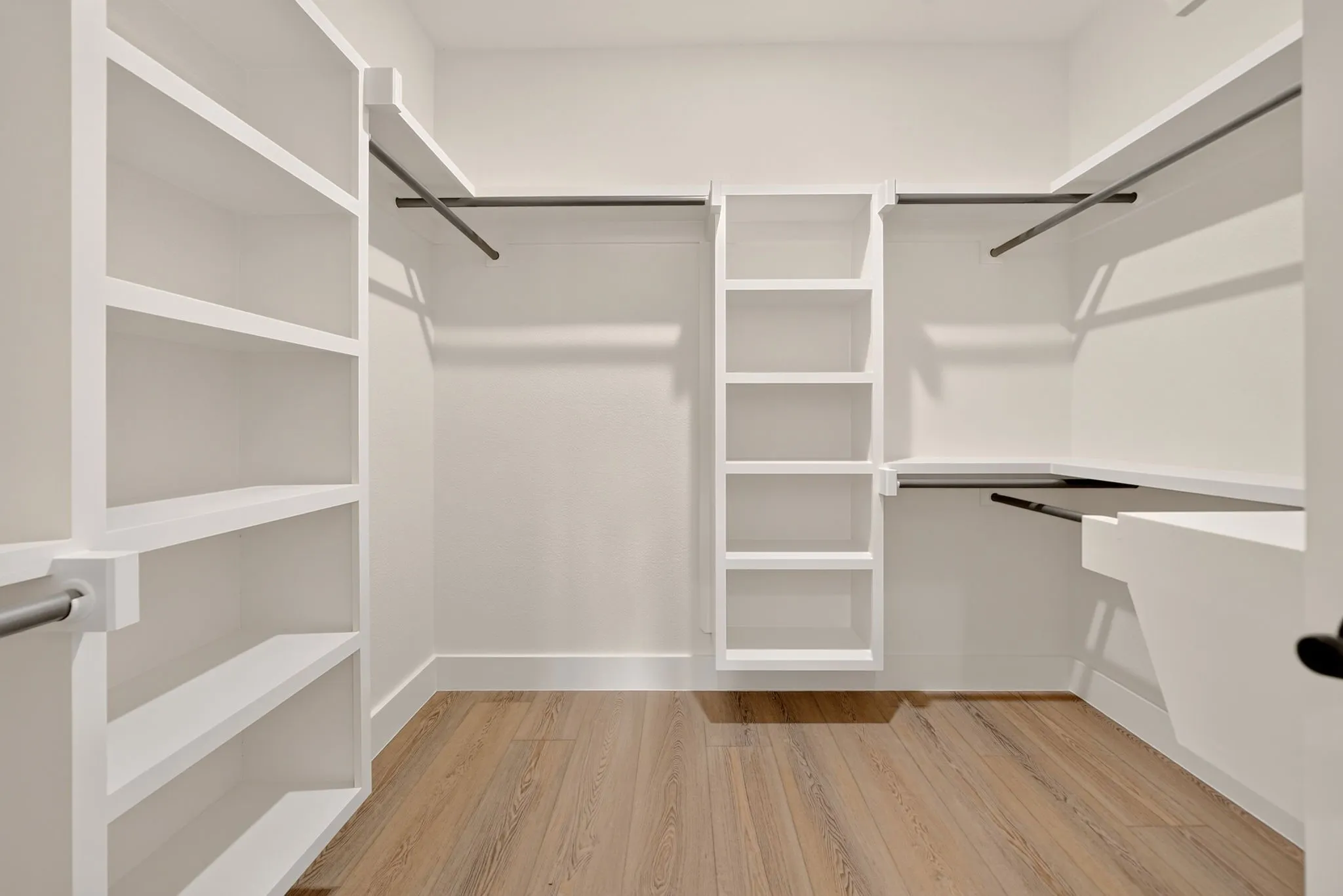 Custom built-in shelving, white cabinetry, wood-finish flooring, and hanging rods