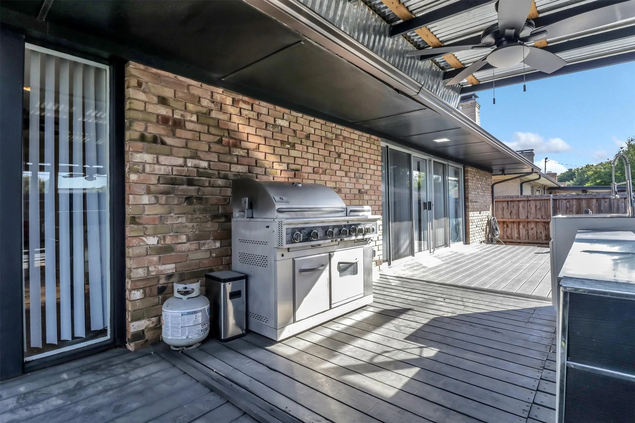 Covered outdoor patio featuring a corrugated metal ceiling with a ceiling fan, a brick exterior wall, and wood-finish decking