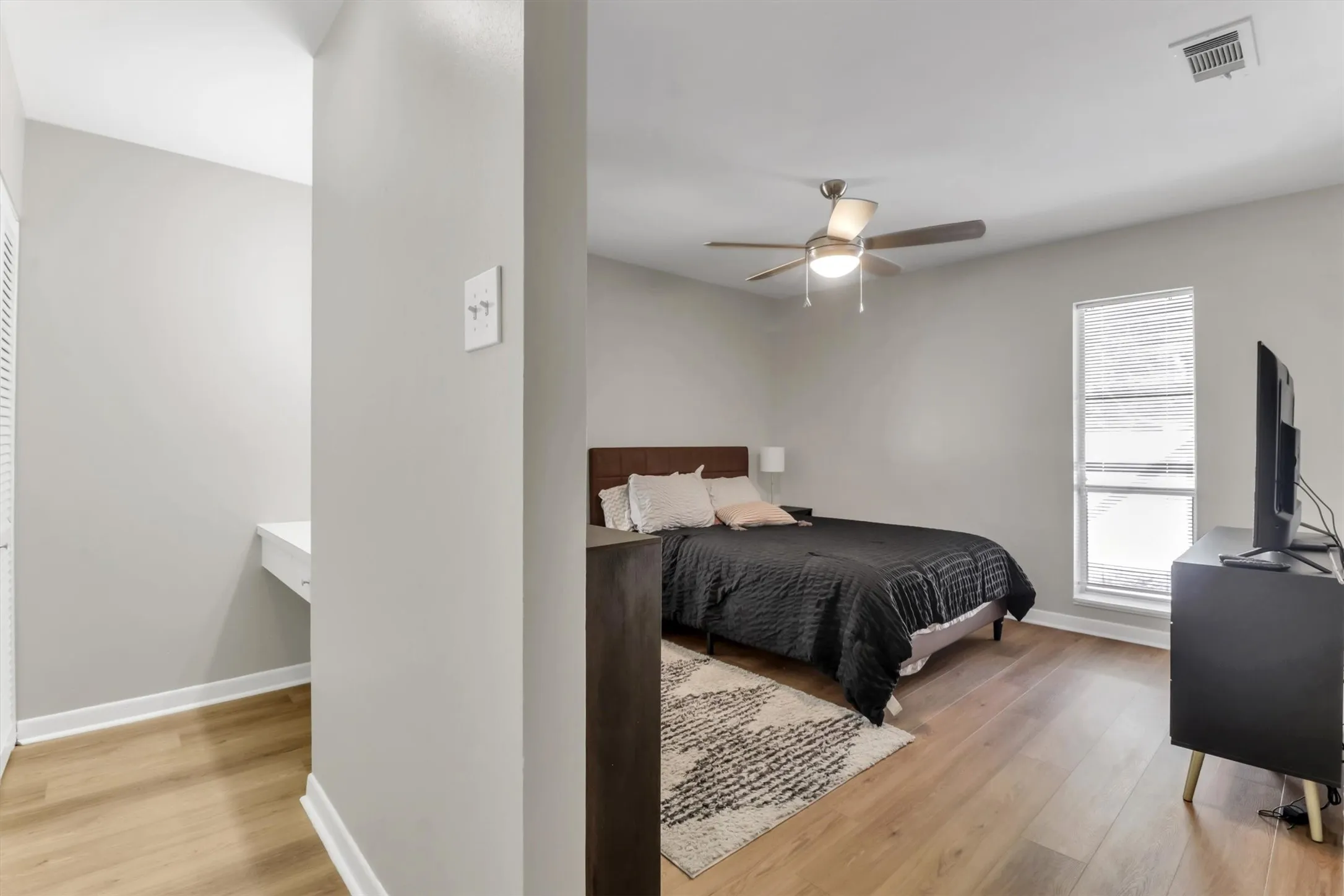 Bedroom with wood-finish flooring, a ceiling fan, and a built-in desk area