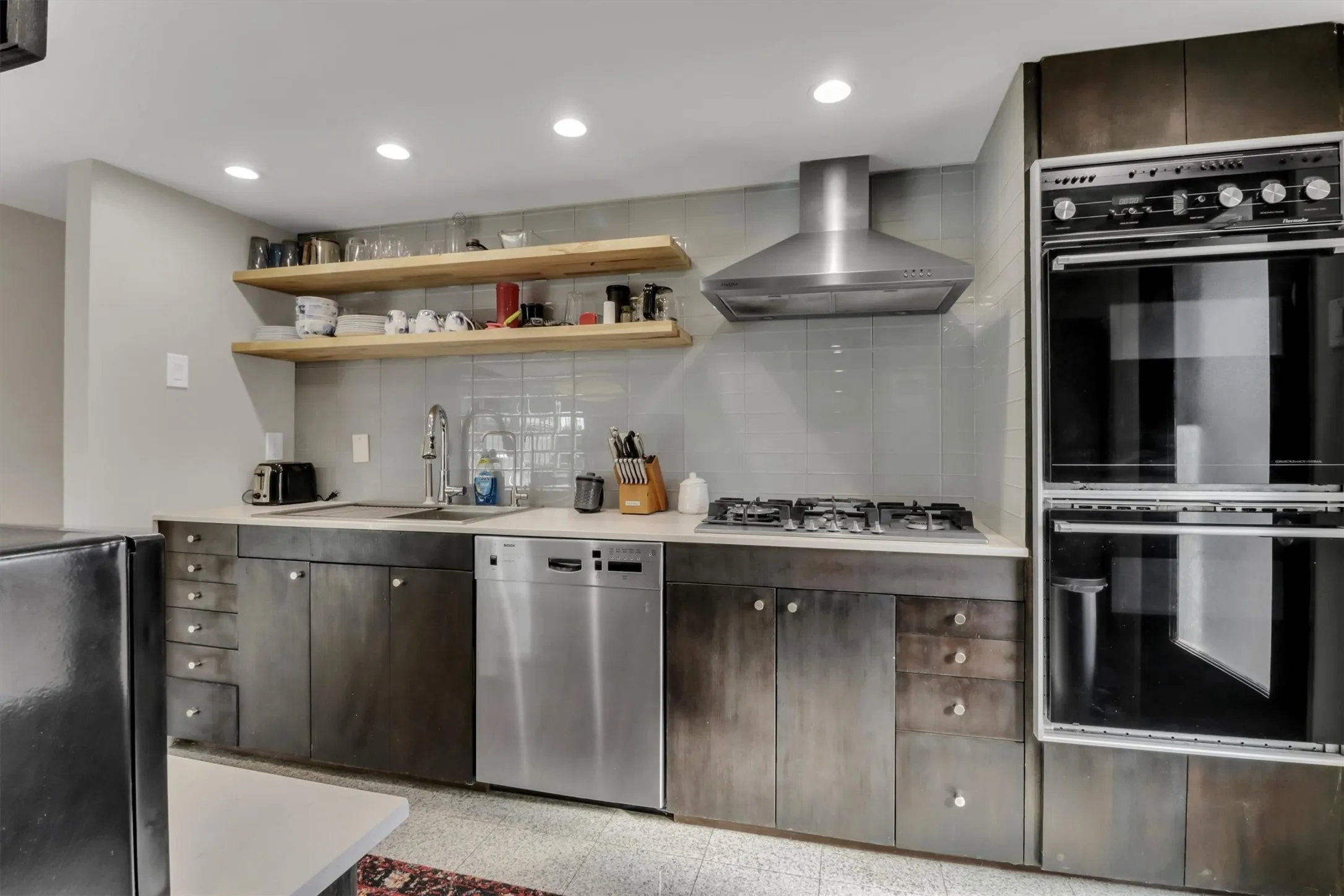 Kitchen featuring stainless steel appliances, recessed lighting, double wall ovens, a gas cooktop with a range hood, and open wood shelving