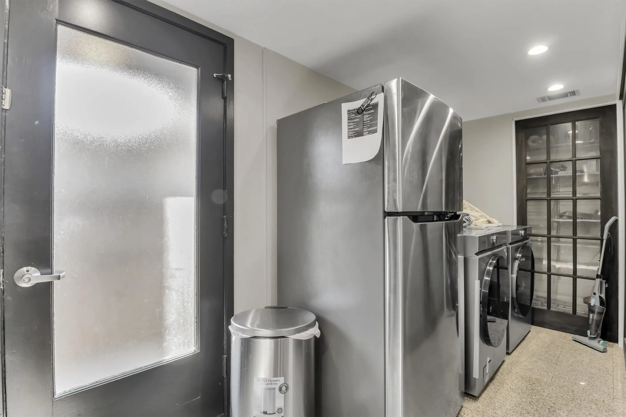 Utility area featuring a stainless steel refrigerator, front-loading washer and dryer, and a grid-patterned glass door