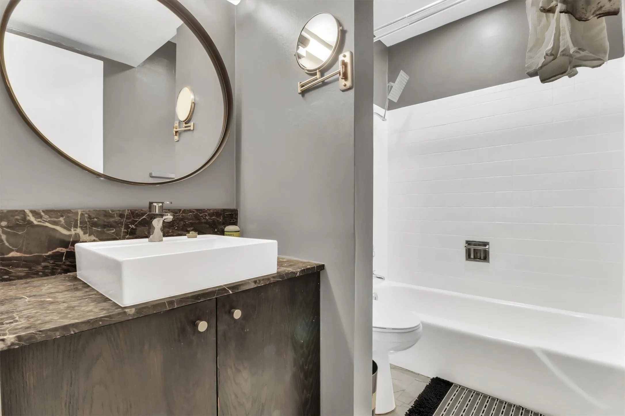 Bathroom vanity featuring a rectangular vessel sink, stone countertop, wood-finish cabinetry, and a circular mirror
