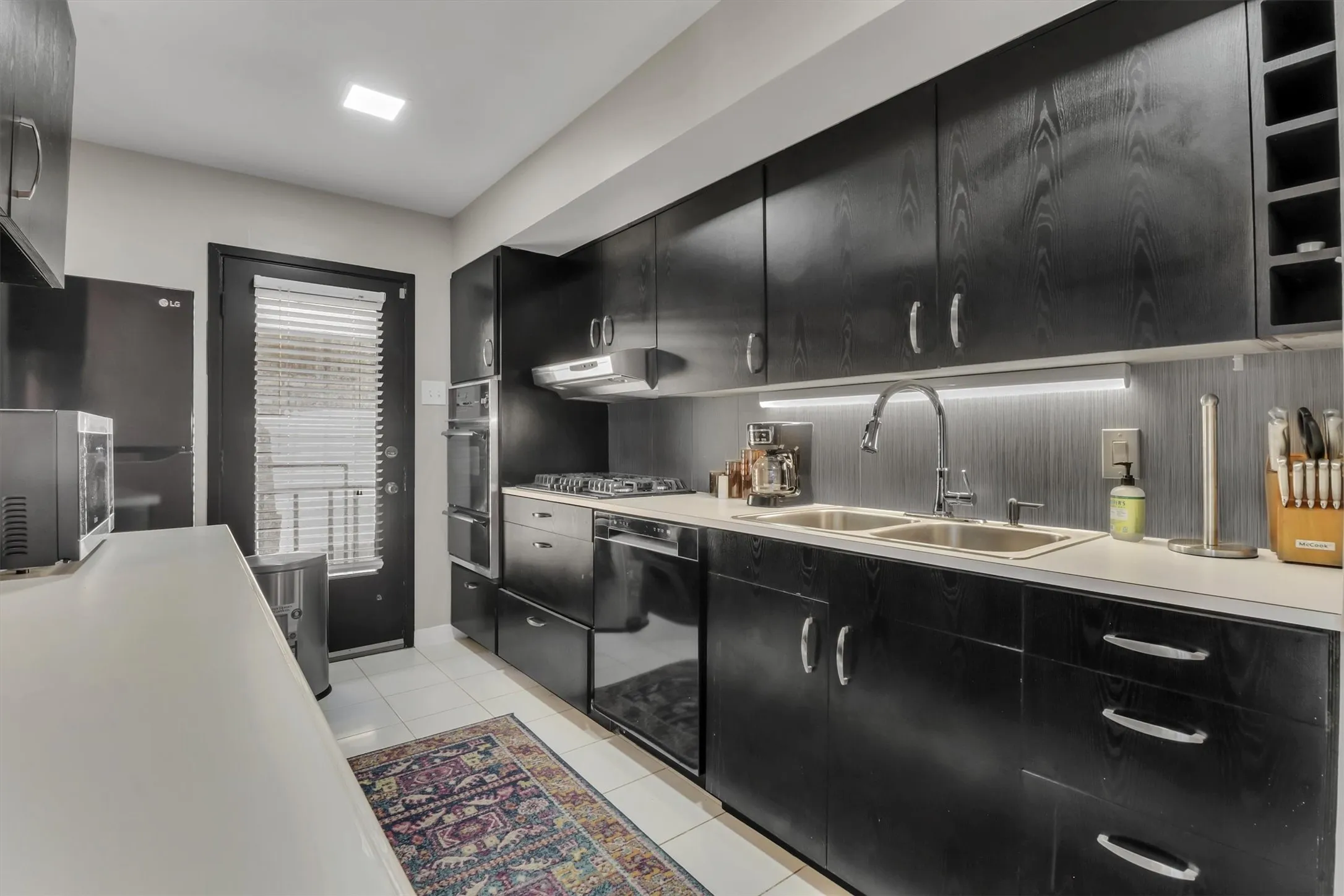 Kitchen featuring dark wood-finish cabinetry, white countertops, dual basin stainless steel sink with a gooseneck faucet, built-in wall oven, and a gas cooktop