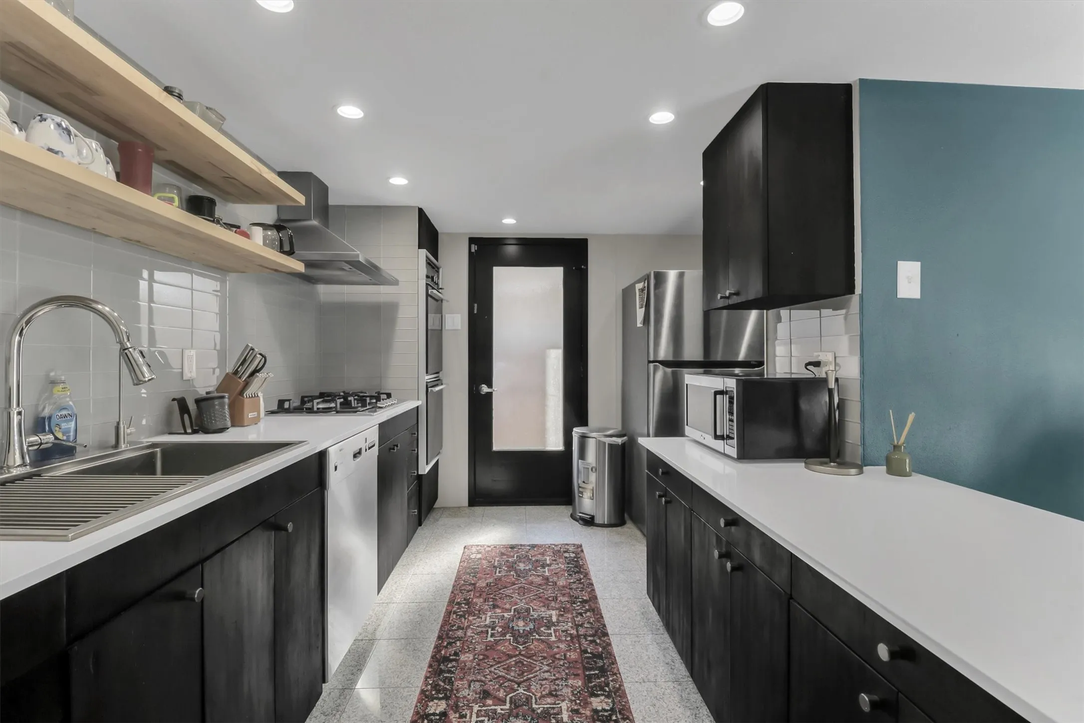 Galley kitchen featuring dark wood-finish cabinetry, light countertops, and a white subway tile backsplash