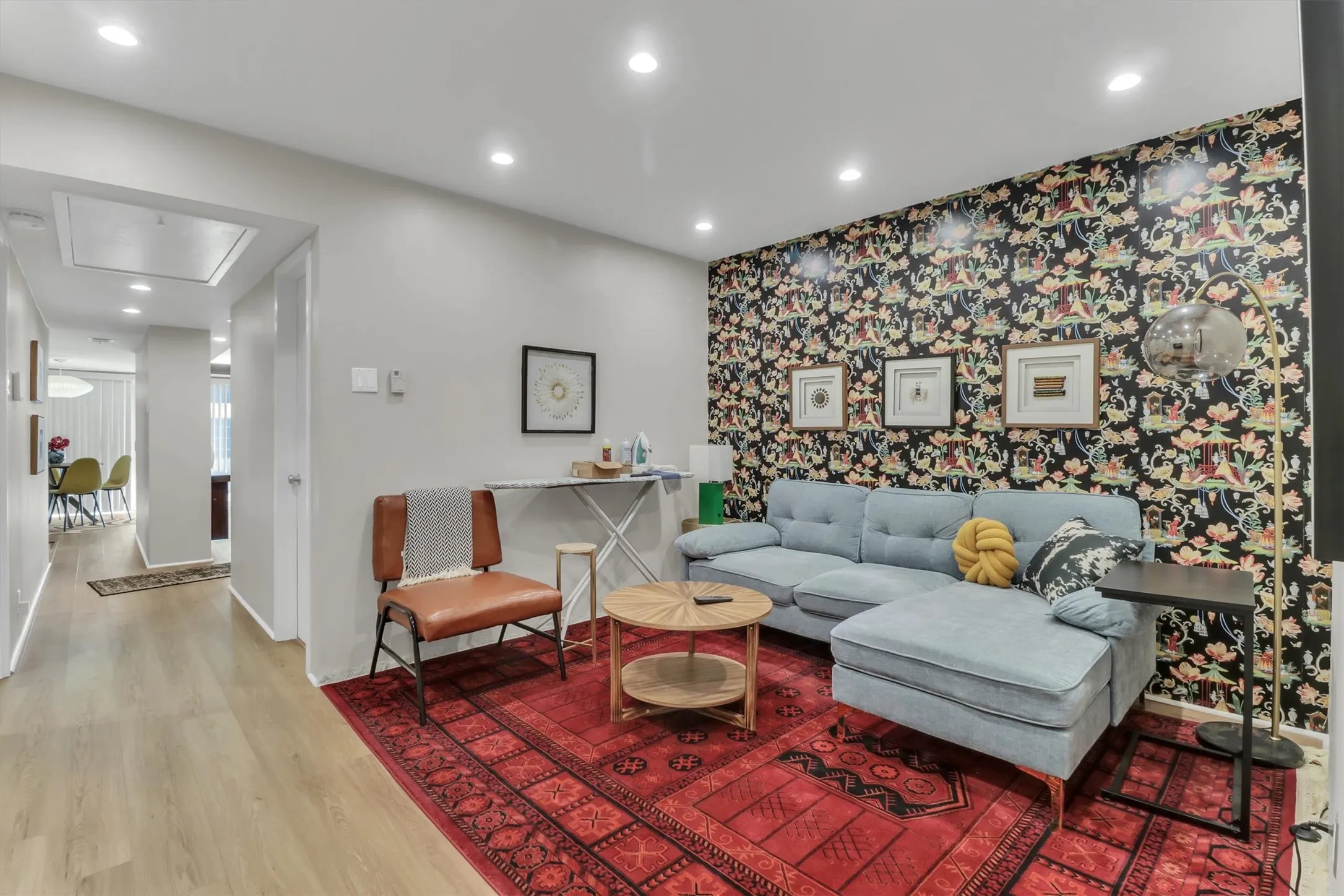 Living area featuring light wood-finish flooring, recessed lighting, and an accent wall with patterned wallpaper