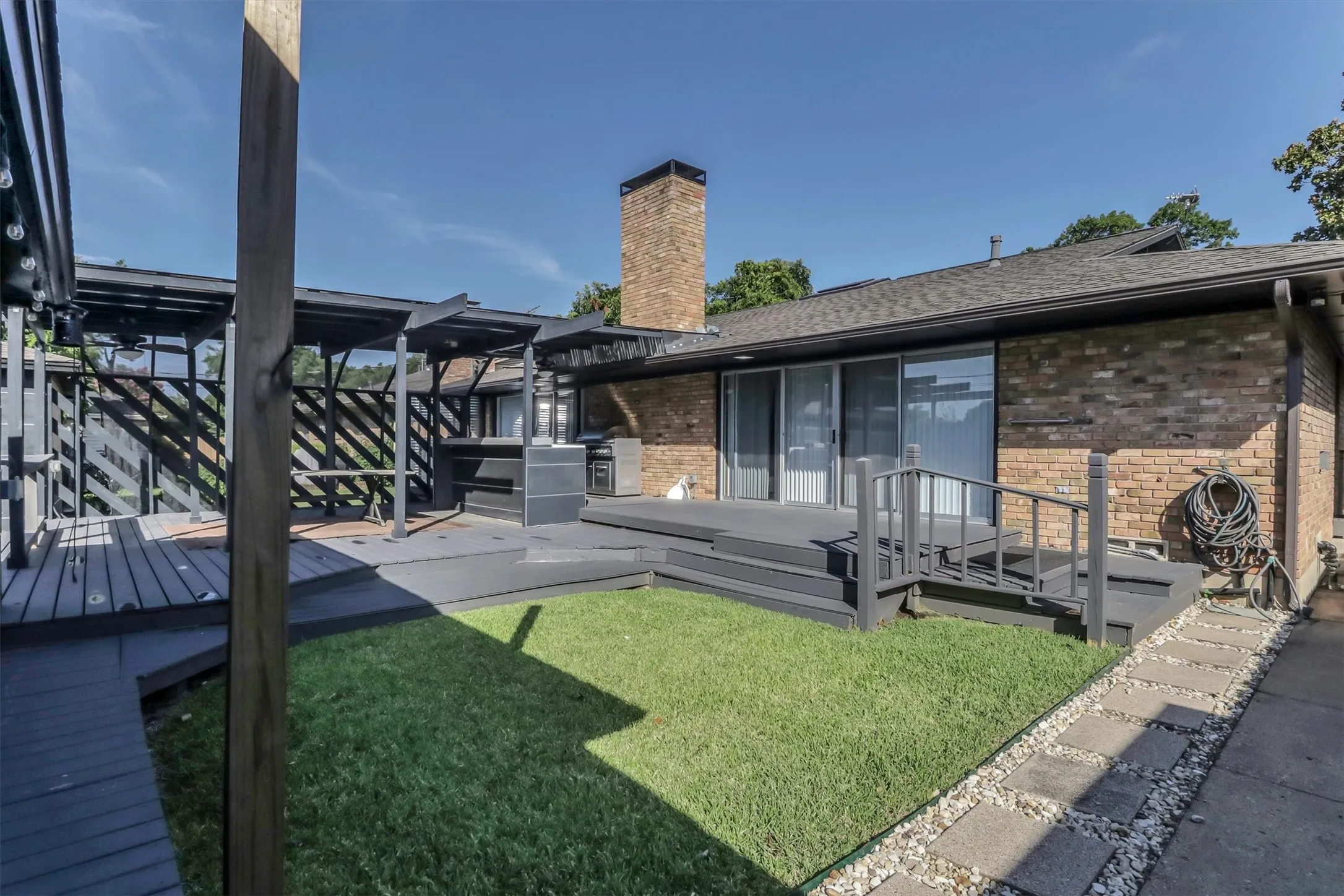 Multi-level deck with built-in pergola structures, integrated outdoor kitchen, and sliding glass door access