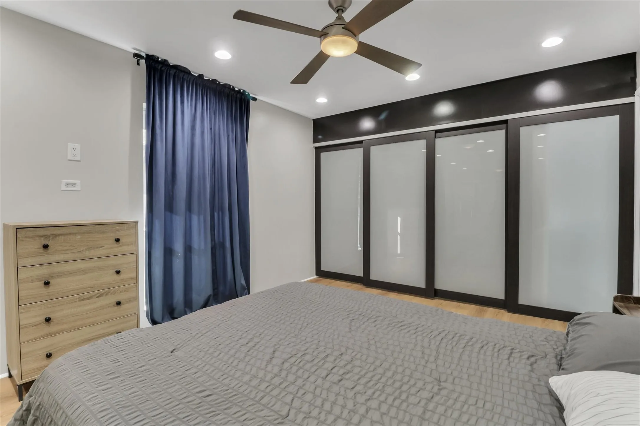 Spacious bedroom featuring light wood-finish flooring, a ceiling fan with integrated lighting, and recessed ceiling lights