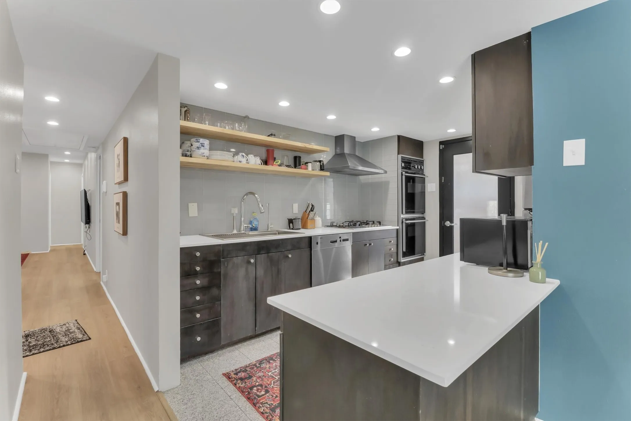 Modern kitchen featuring dark wood-finish cabinetry, stainless steel appliances including a built-in oven and dishwasher, and a white countertop island
