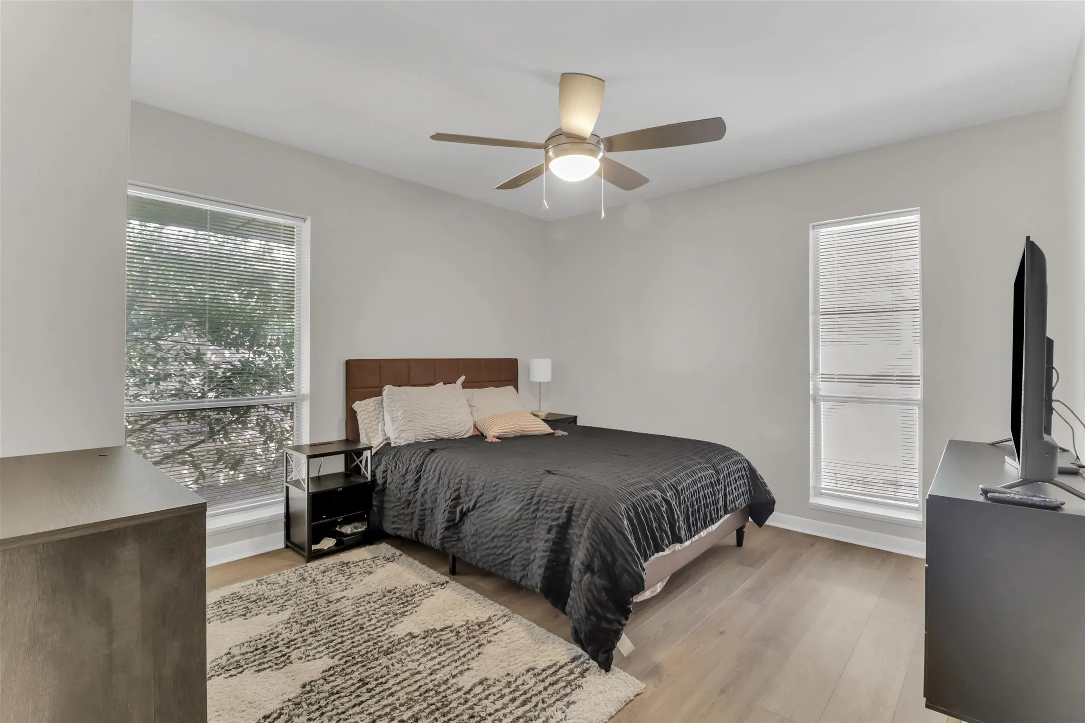 Bedroom featuring wood-finish flooring, light grey walls, and a ceiling fan with integrated lighting