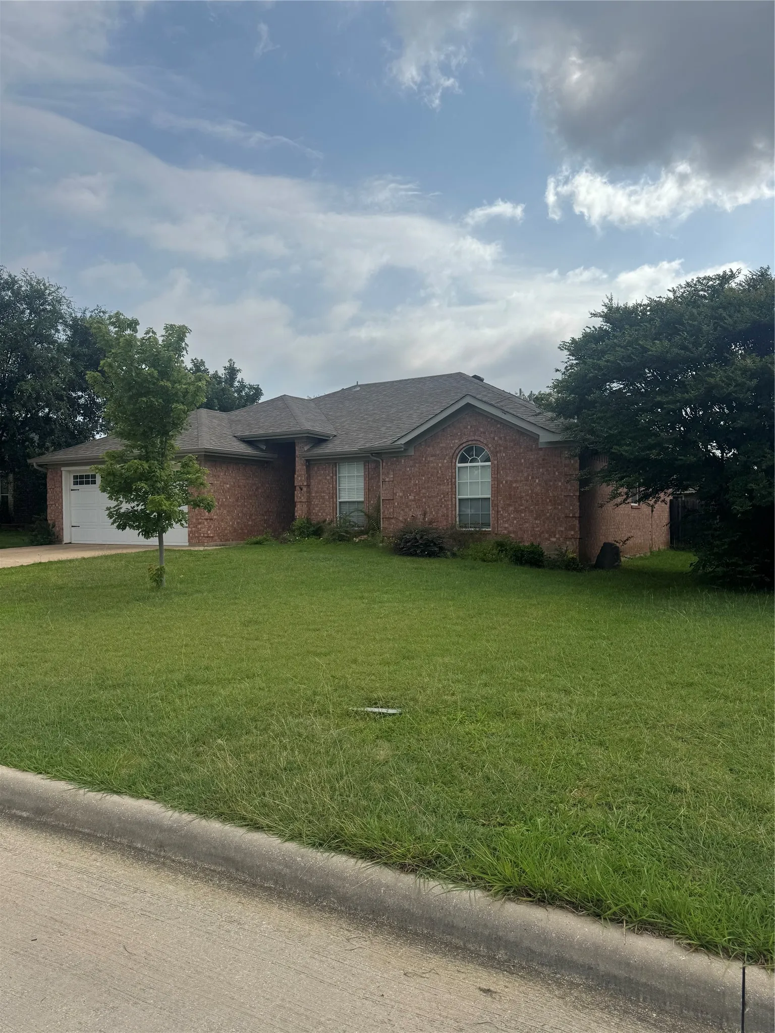 Brick exterior featuring a two-car garage with a panel door, a gabled roofline, and established landscaping