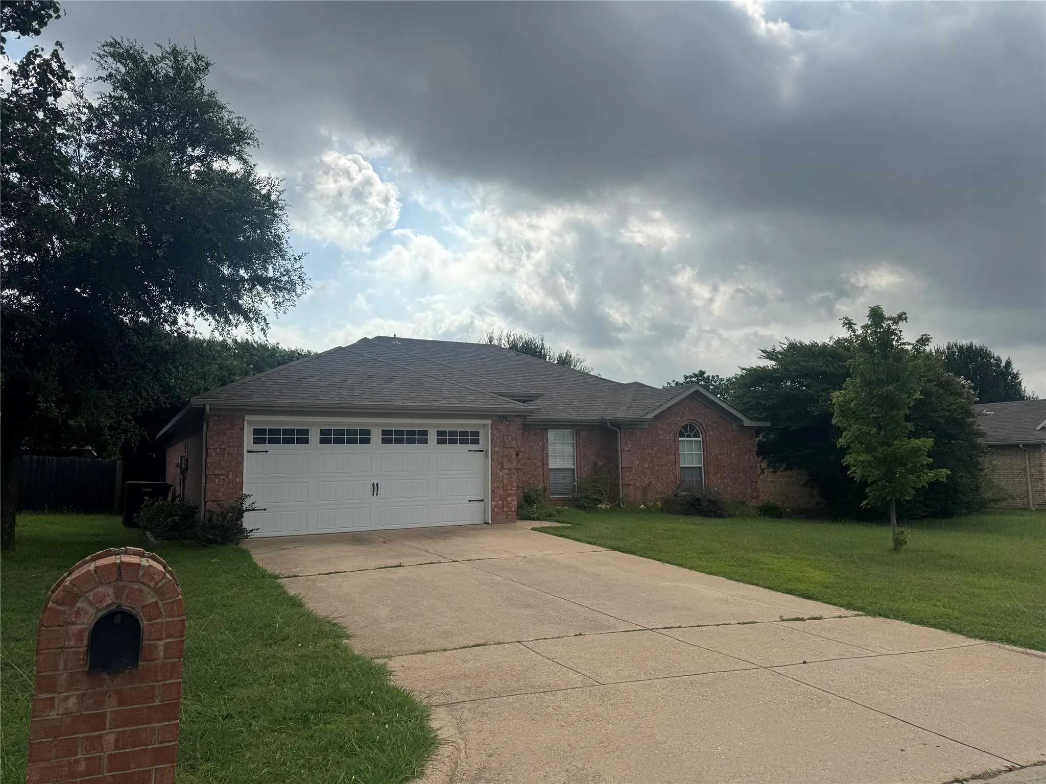 Brick exterior featuring a two-car garage with paneling and window inserts, a paved driveway, and a shingled roof