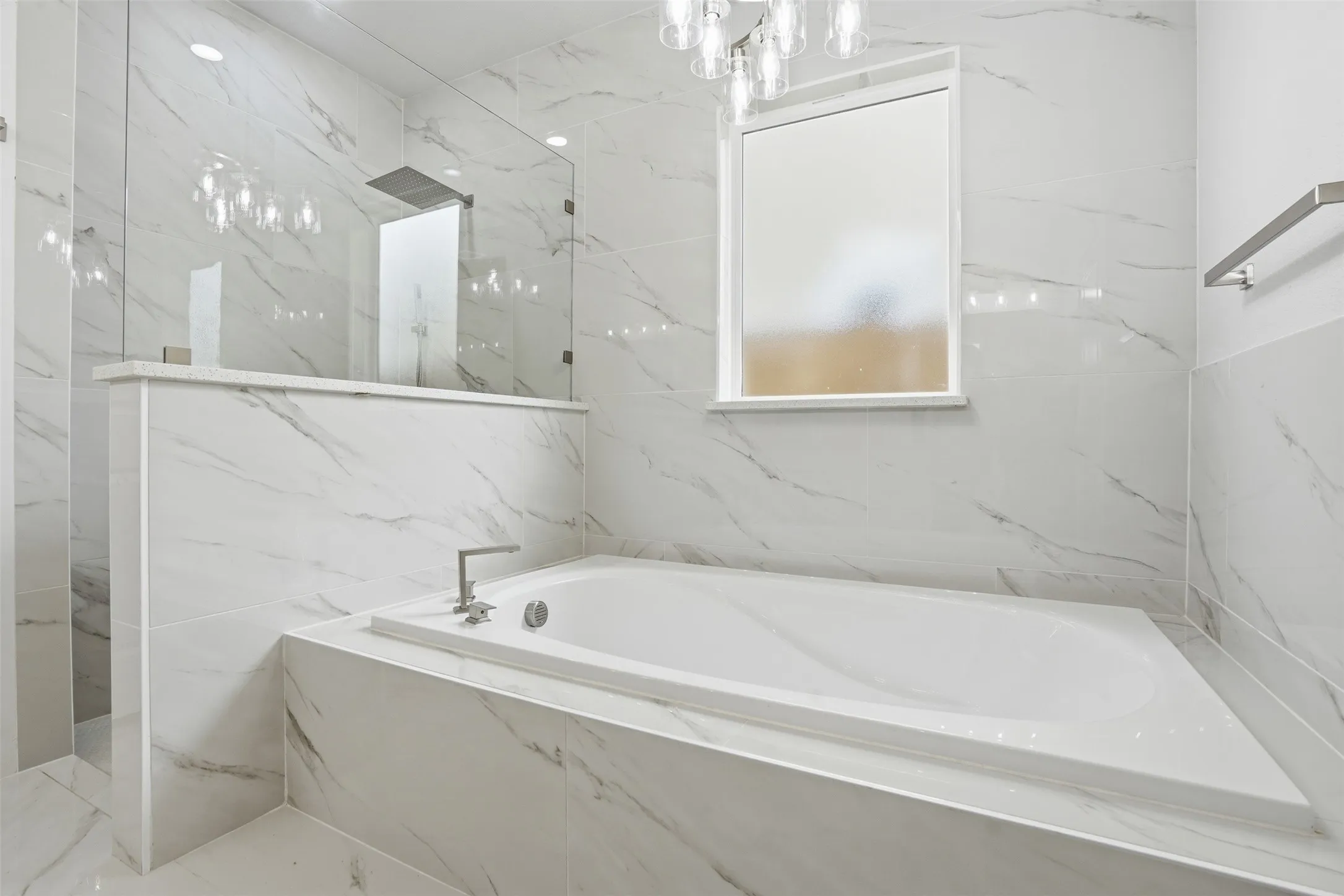 Built-in soaking tub with a deck-mounted faucet set, surrounded by large format tile with subtle veining