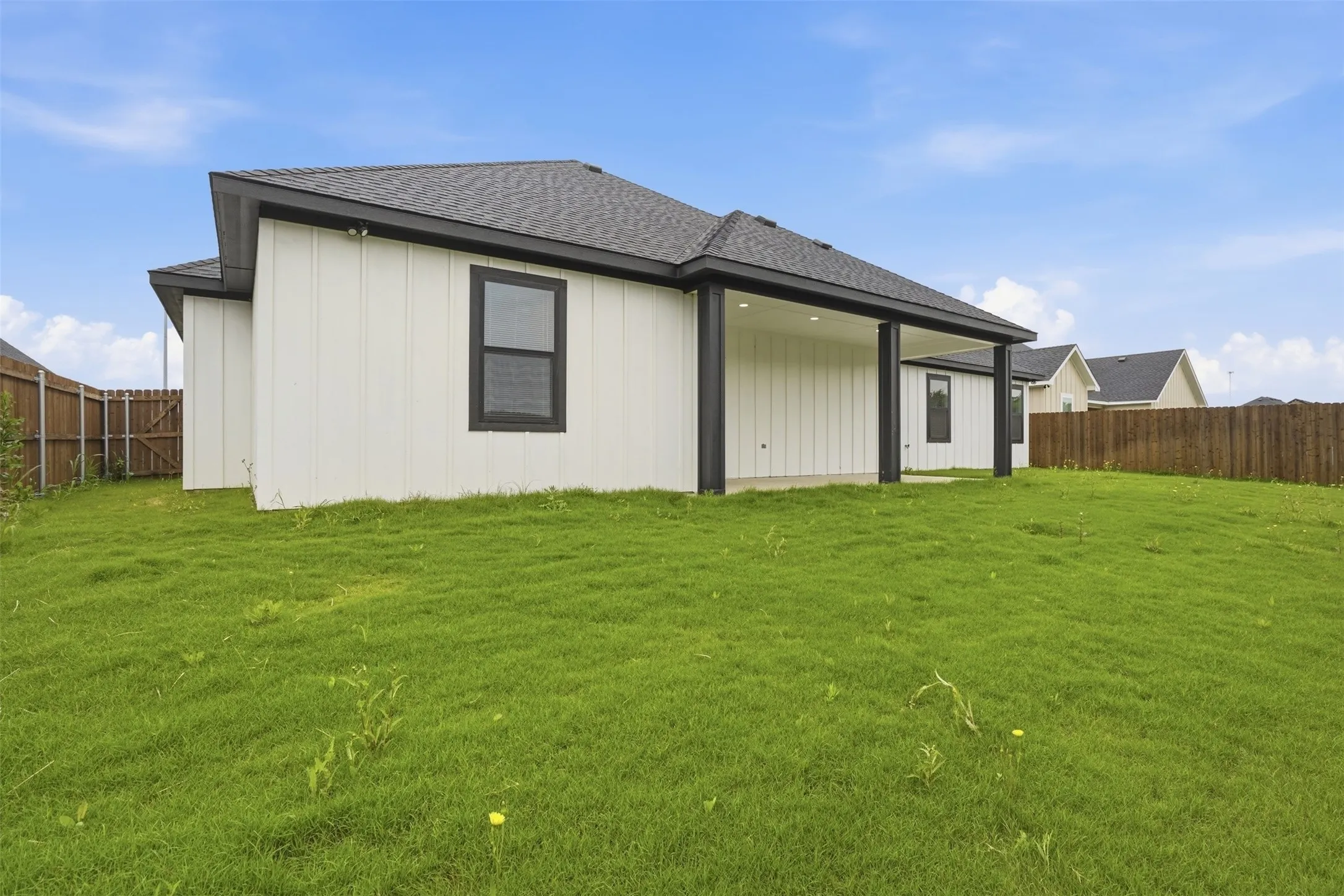 Expansive backyard featuring a covered patio, board and batten siding, dark-framed windows, a dark shingled roof, and perimeter wood fencing